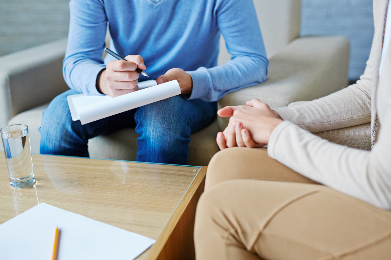Two people in a counseling session, one taking notes on a clipboard beside a coffee table