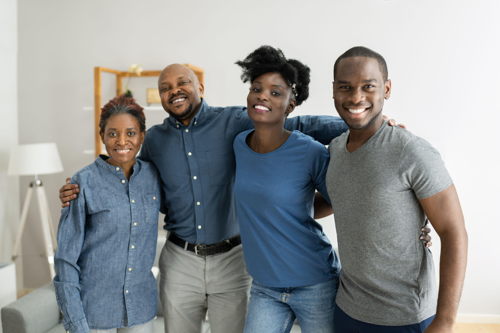 Four smiling people standing together in a bright living room, arms around each other.