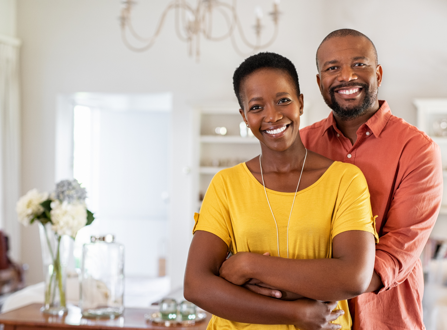 Smiling couple standing together in a bright kitchen, with flowers and decor in the background