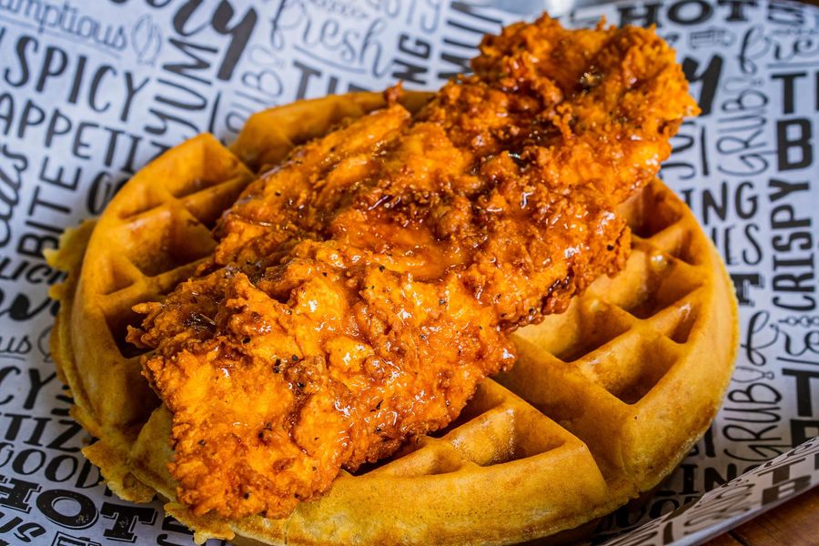 Waffle topped with a crispy fried chicken strip on printed paper