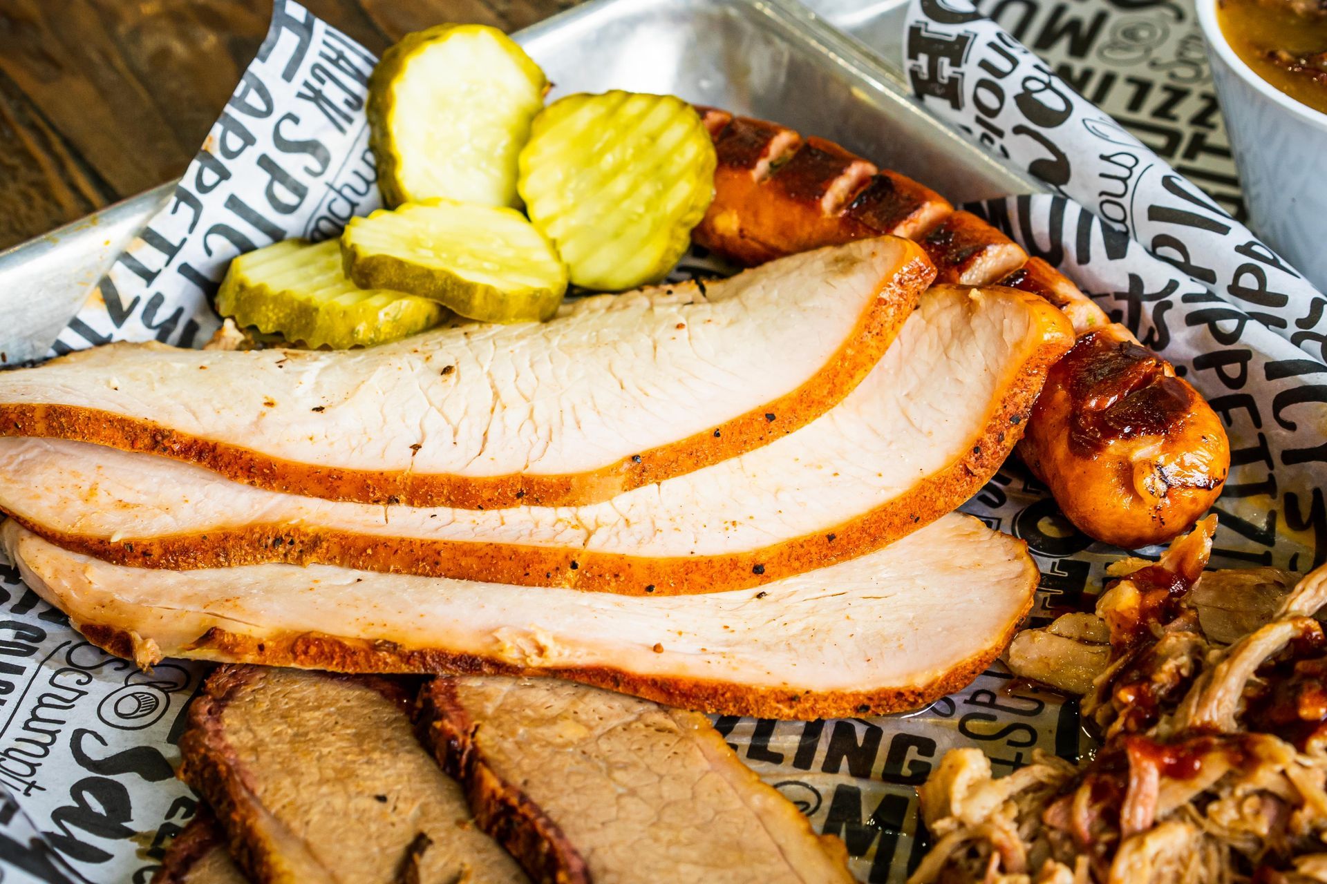 Sliced smoked turkey with pickles on butcher paper, served with grilled onions