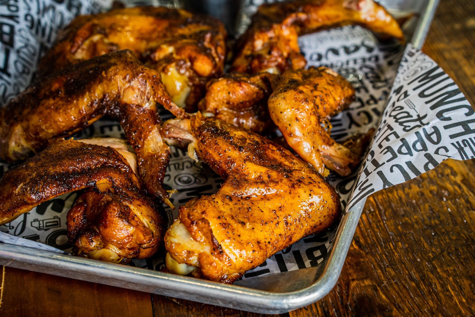 Tray of glazed grilled chicken wings on newspaper-lined paper in a rustic serving basket