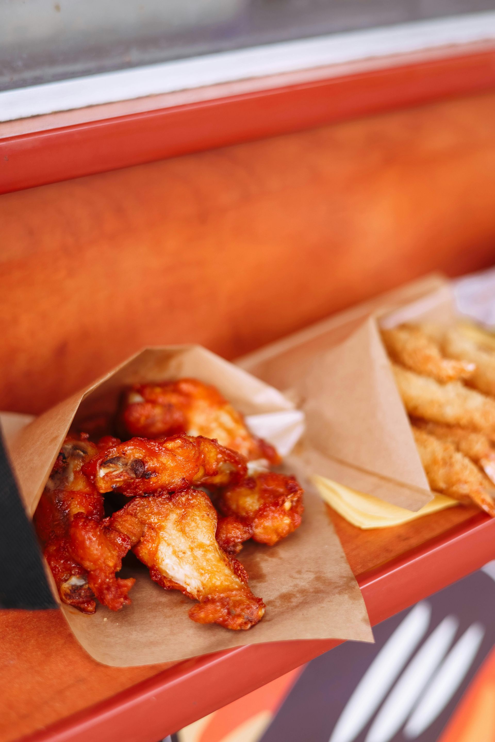 Takeout tray of saucy fried chicken wings and fries on a red counter