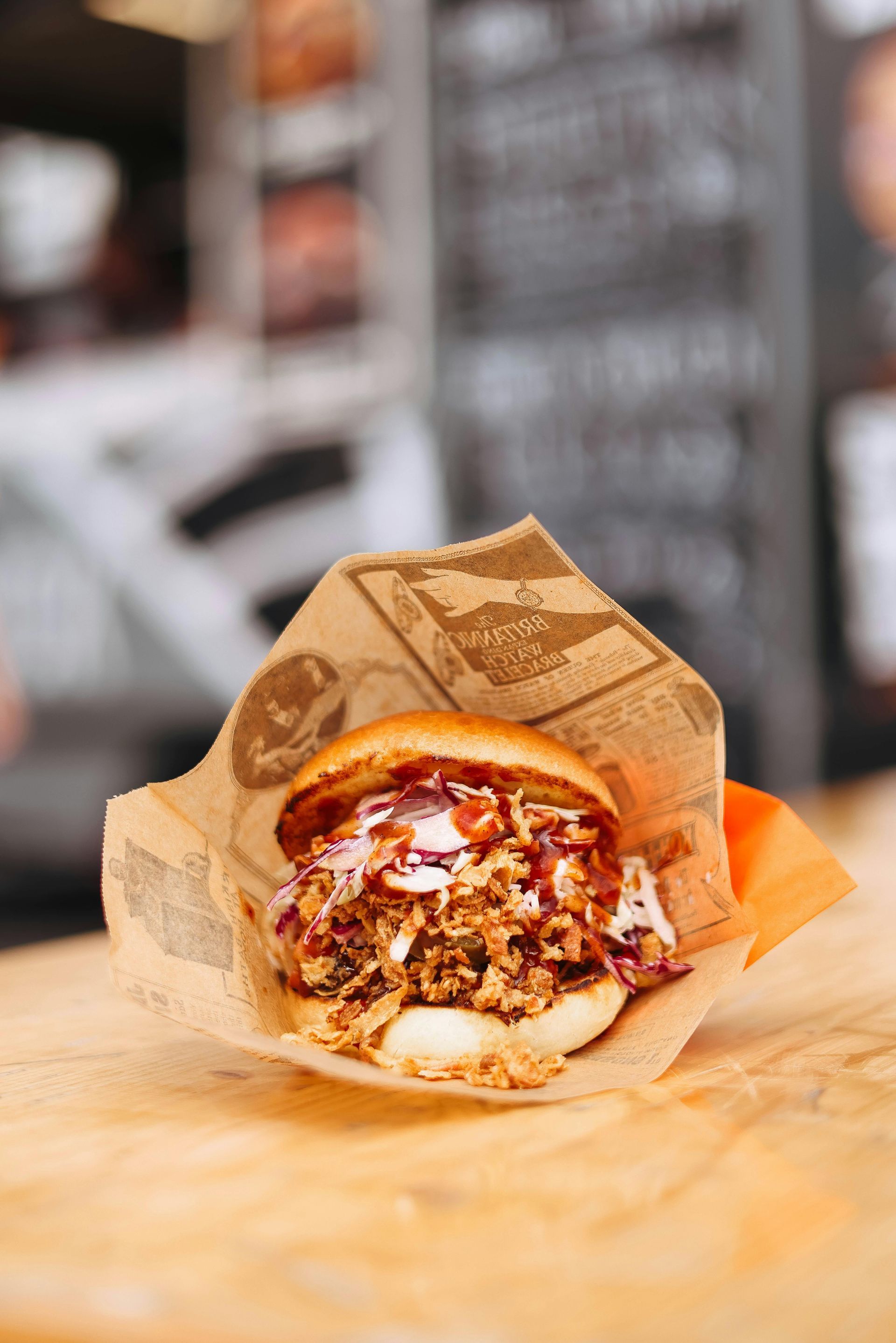 Burger in a paper wrapper on a wooden table with melted cheese and sauce in a restaurant setting