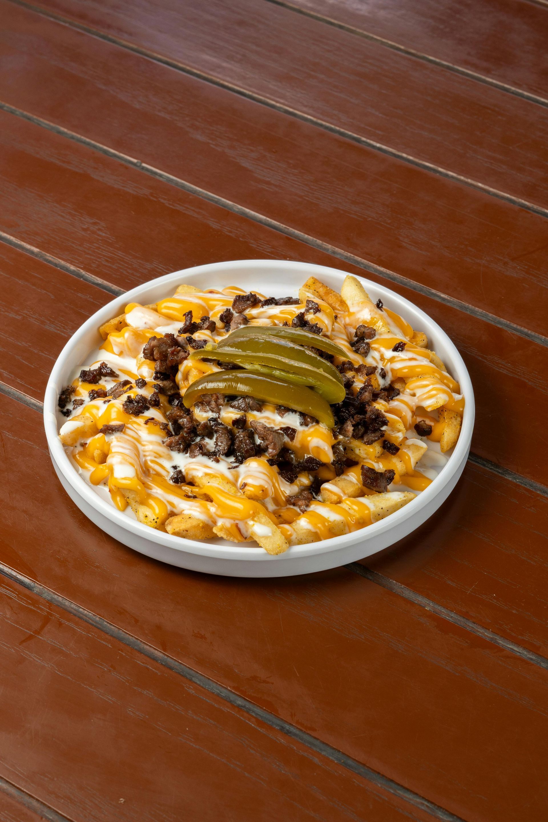 Plate of loaded fries topped with cheese, beef, and pickles on a wooden table