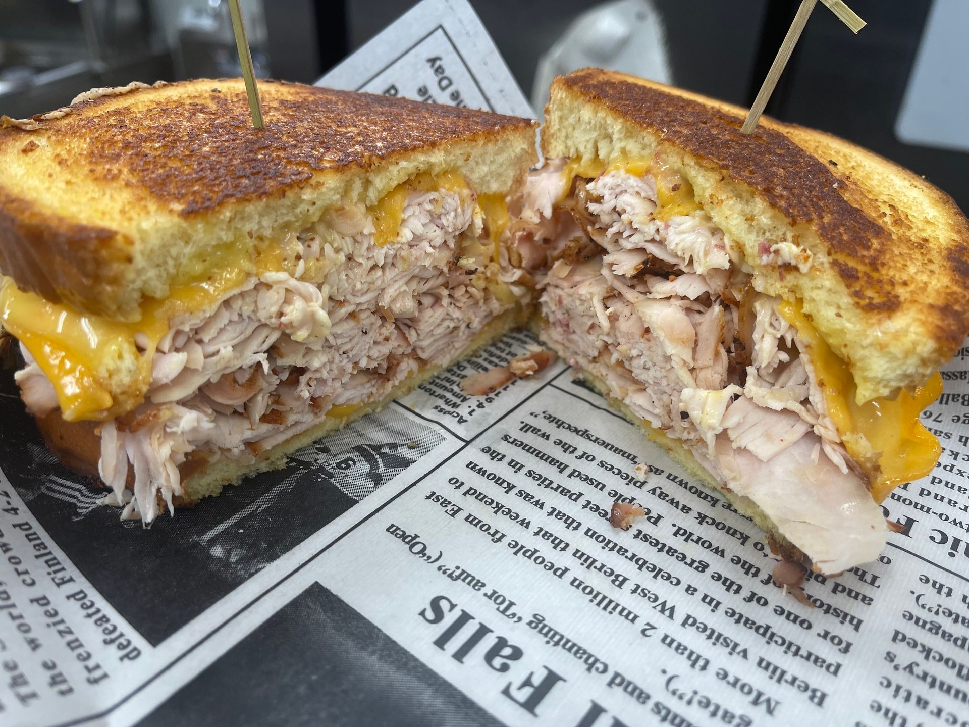 Grilled cheese sandwich with melted cheddar and shredded meat, cut in half on newspaper-lined tray