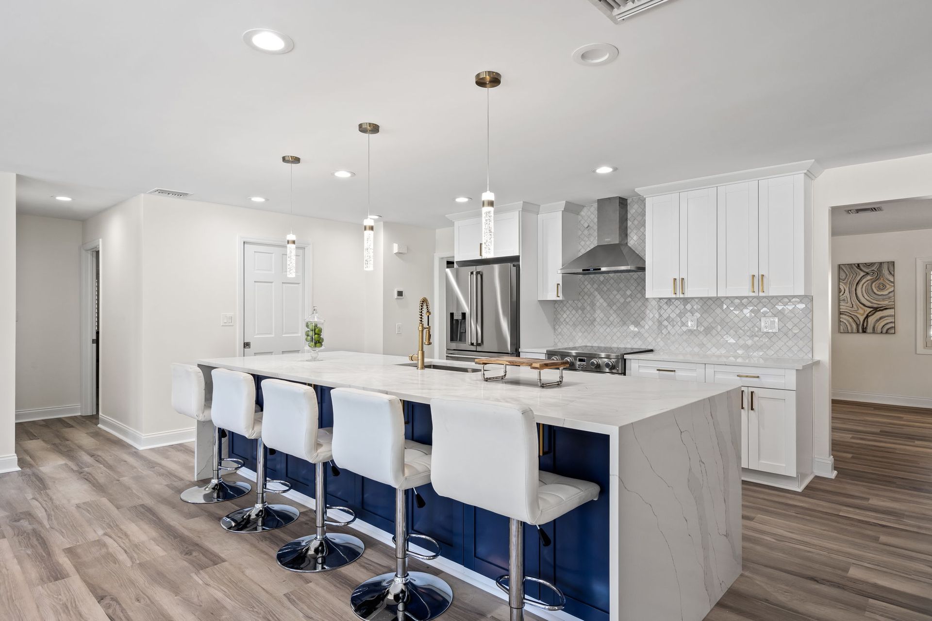 Bright modern kitchen with a large island, white cabinets, bar stools, and stainless steel appliances