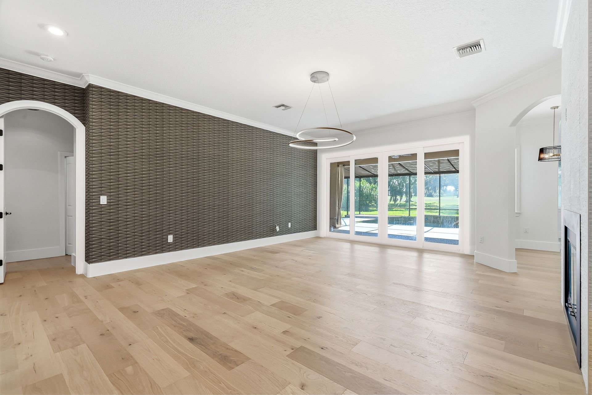Living room with woven-texture accent wall and wood-look flooring, opening to a covered lanai and pool
