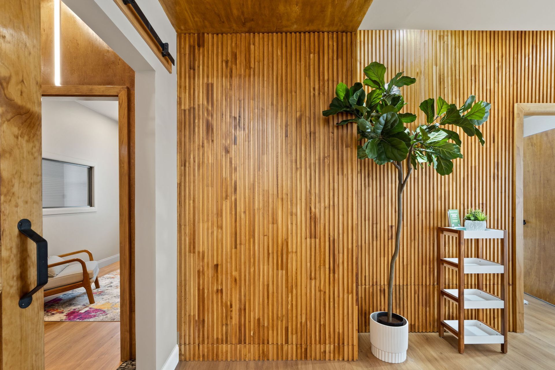 Modern hallway with wood slat walls, potted tree, mirror, and white shelf.