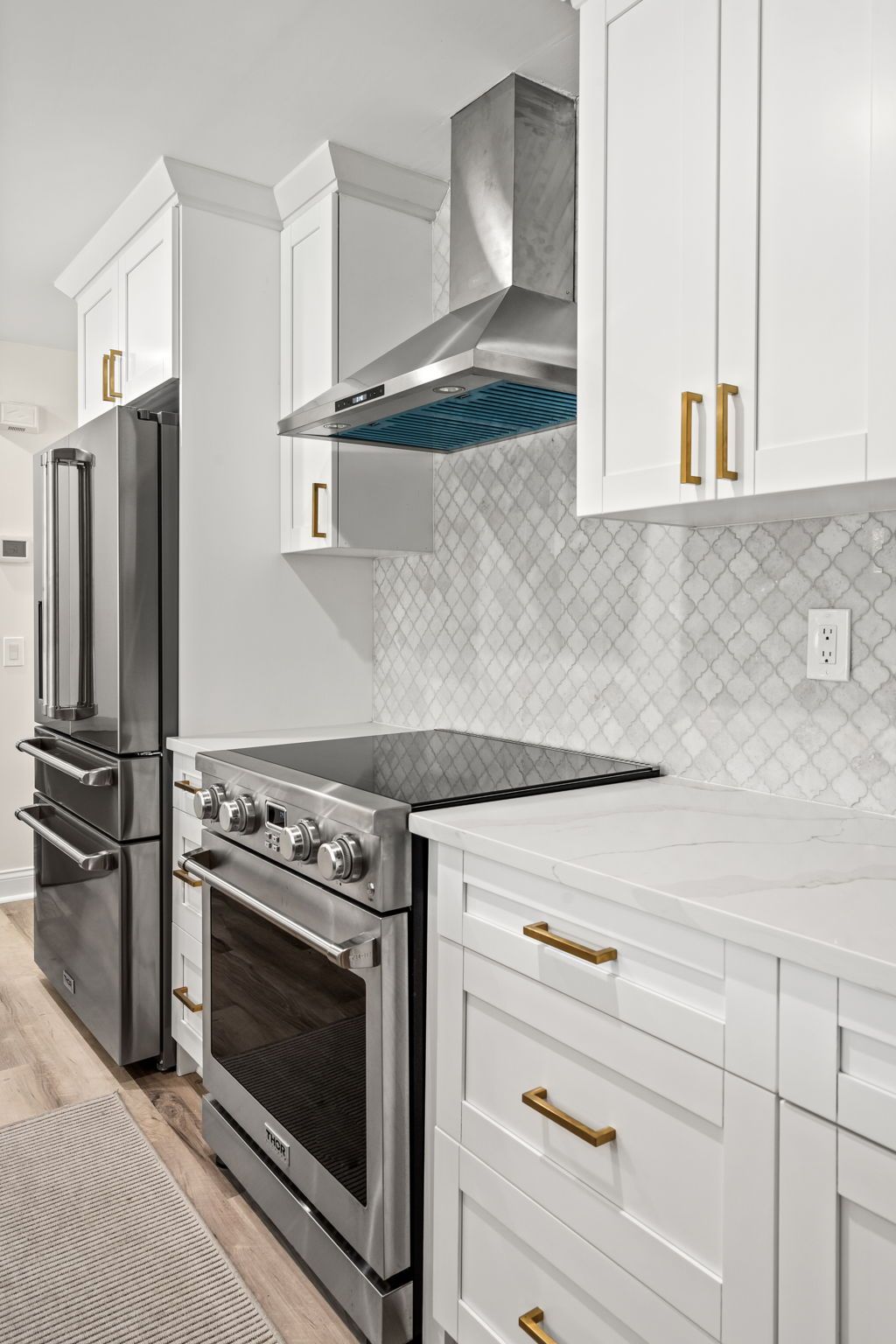 Modern white kitchen with stainless steel appliances, white cabinets, and gold handles