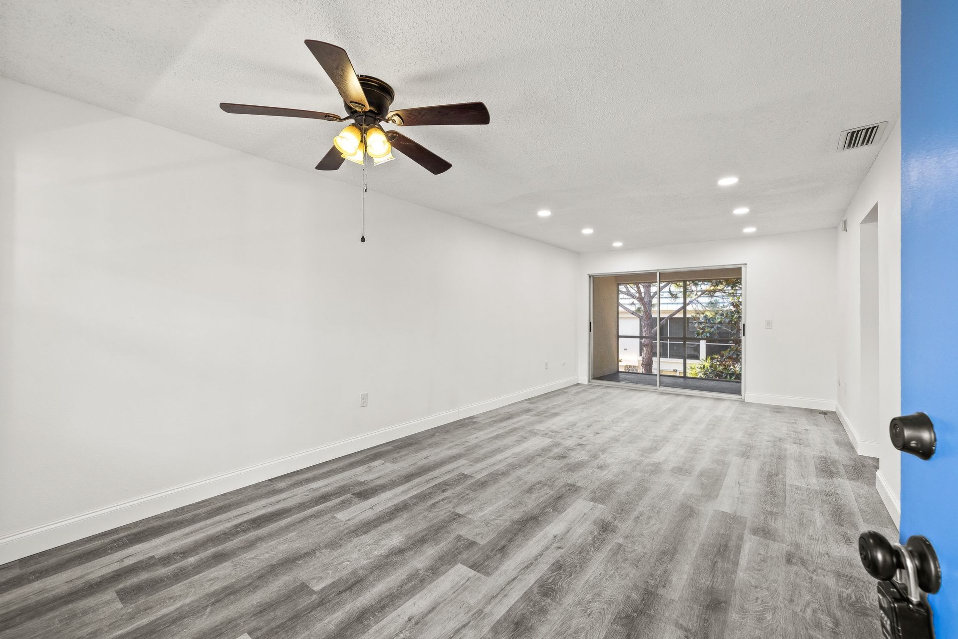 Empty white living room with gray carpet, ceiling fan, recessed lights, and sliding glass doors