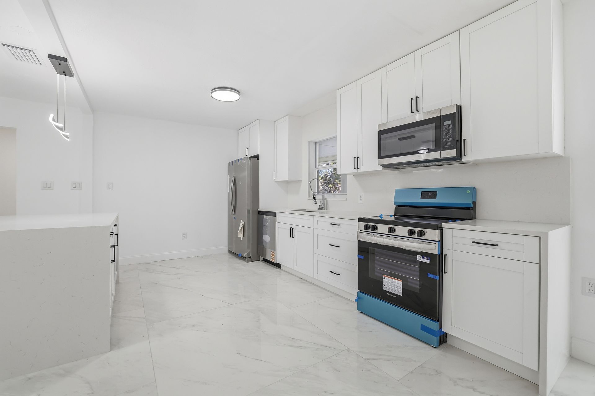 Bright modern kitchen with white cabinets, stainless fridge, blue stove, and marble-style floor