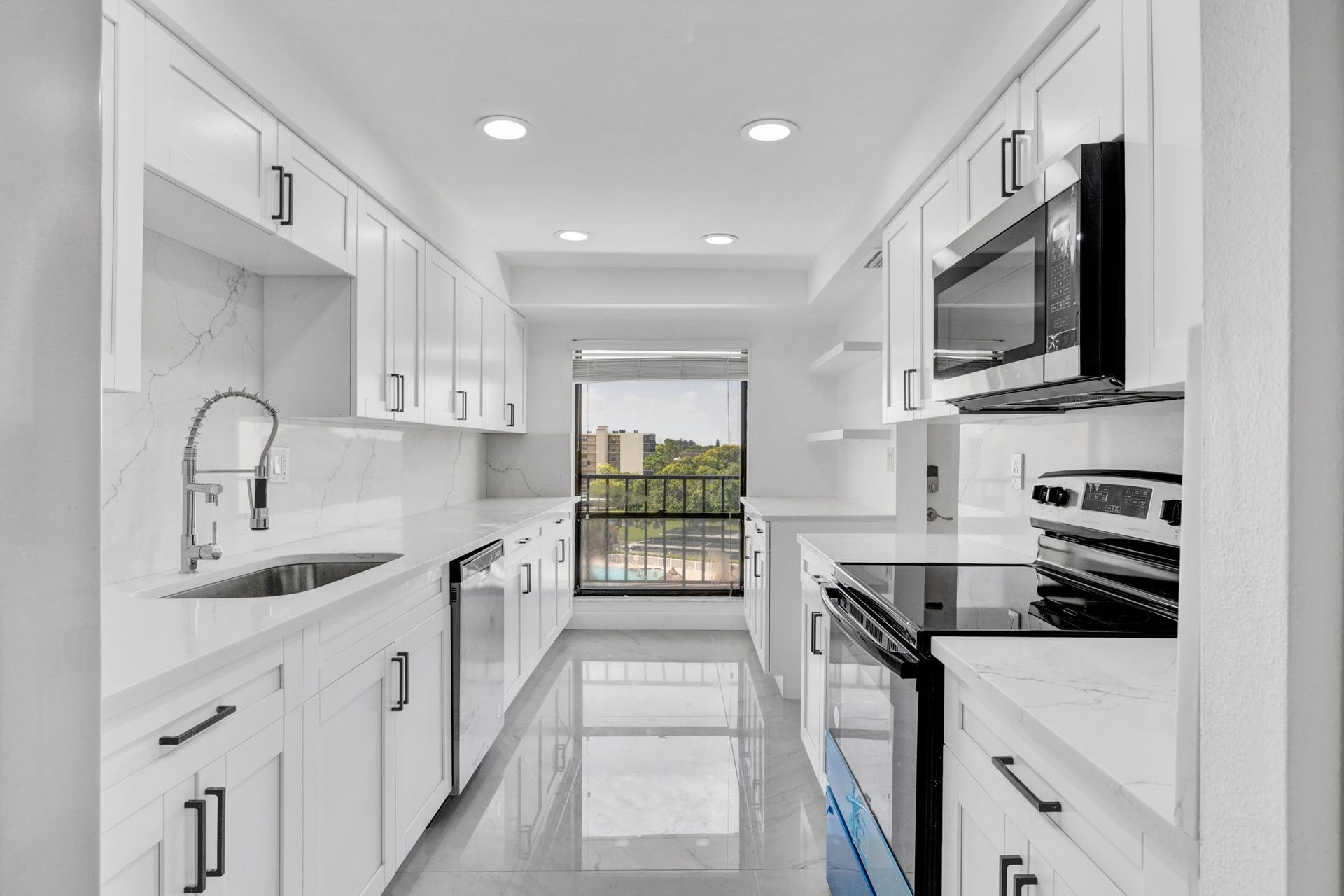 Bright modern white galley kitchen with stainless appliances and a window view of greenery
