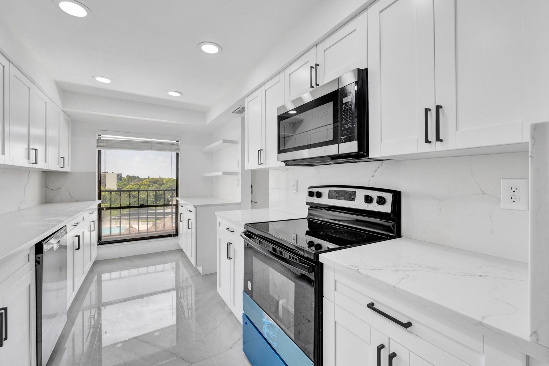 Bright white galley kitchen with stainless appliances, glossy floor, and balcony doors at the end