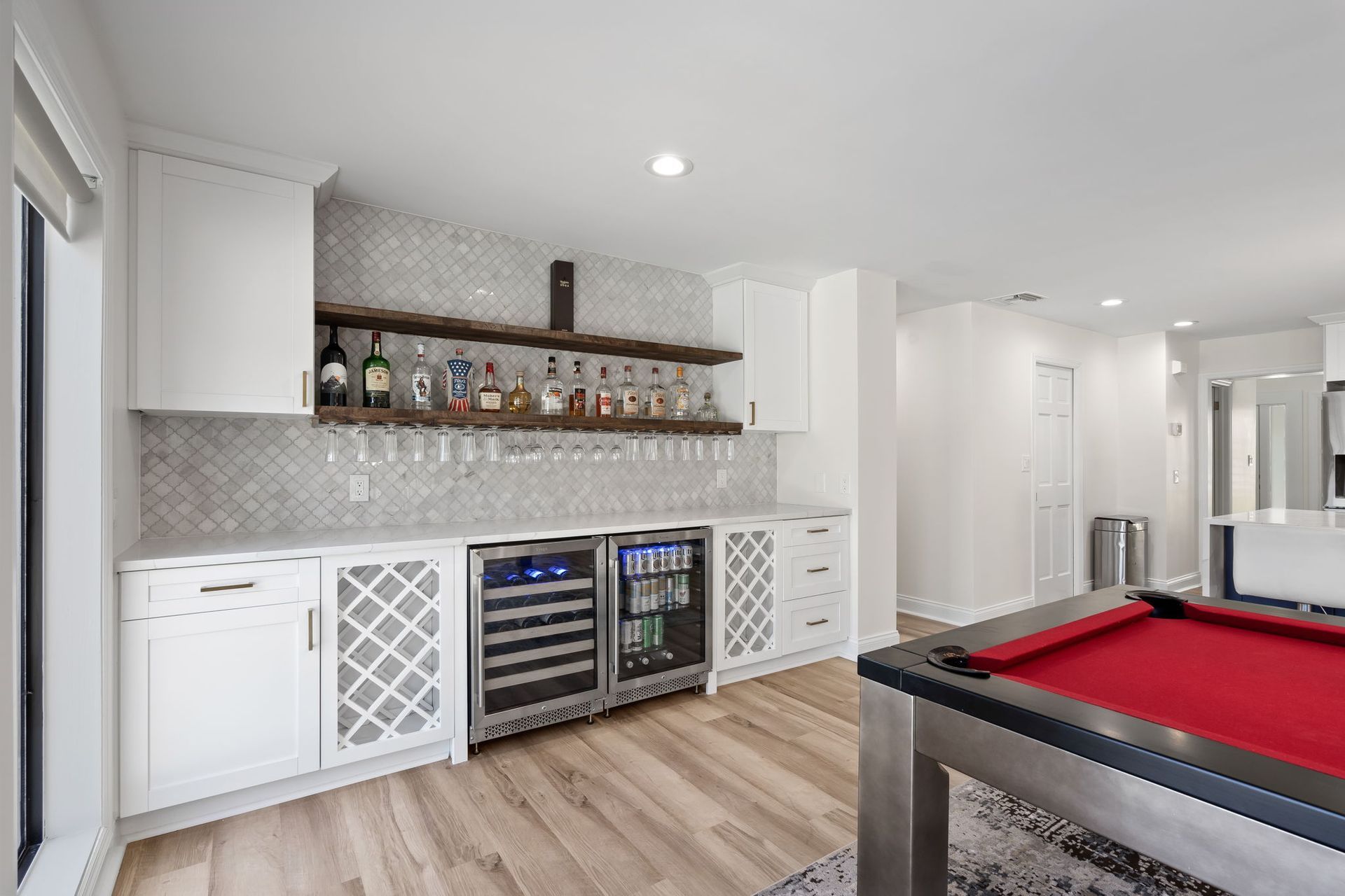 Bright modern rec room with wet bar, wine fridge, white cabinets, and a pool table in the foreground