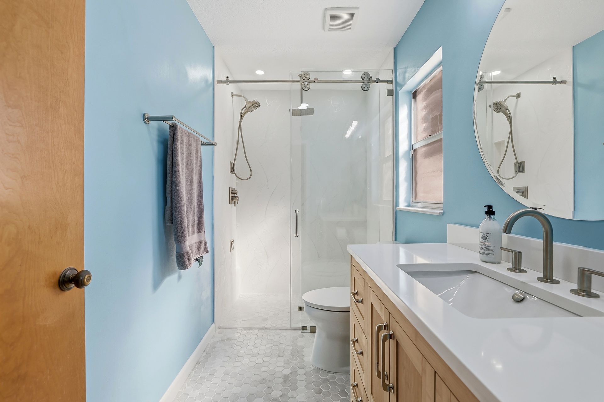 Bright bathroom with blue walls, glass shower, wood vanity, white sink, and towels on the wall.