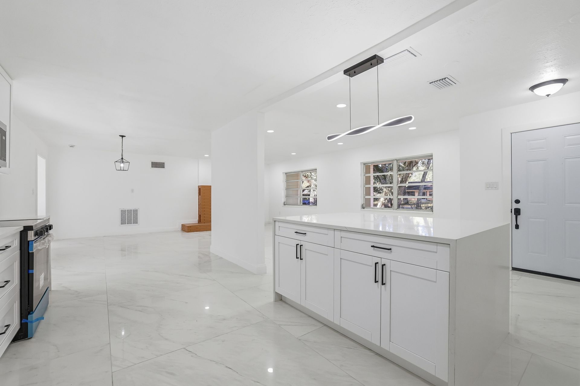 Bright white modern kitchen with island, glossy tile floors, and stainless fixtures in an open-plan home