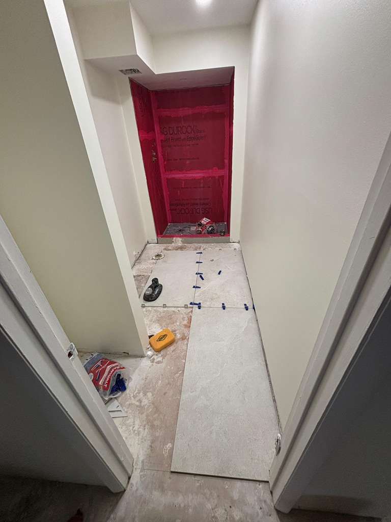 Narrow hallway under renovation with red plastic sheeting at the far end and tools, debris, and boards on the floor