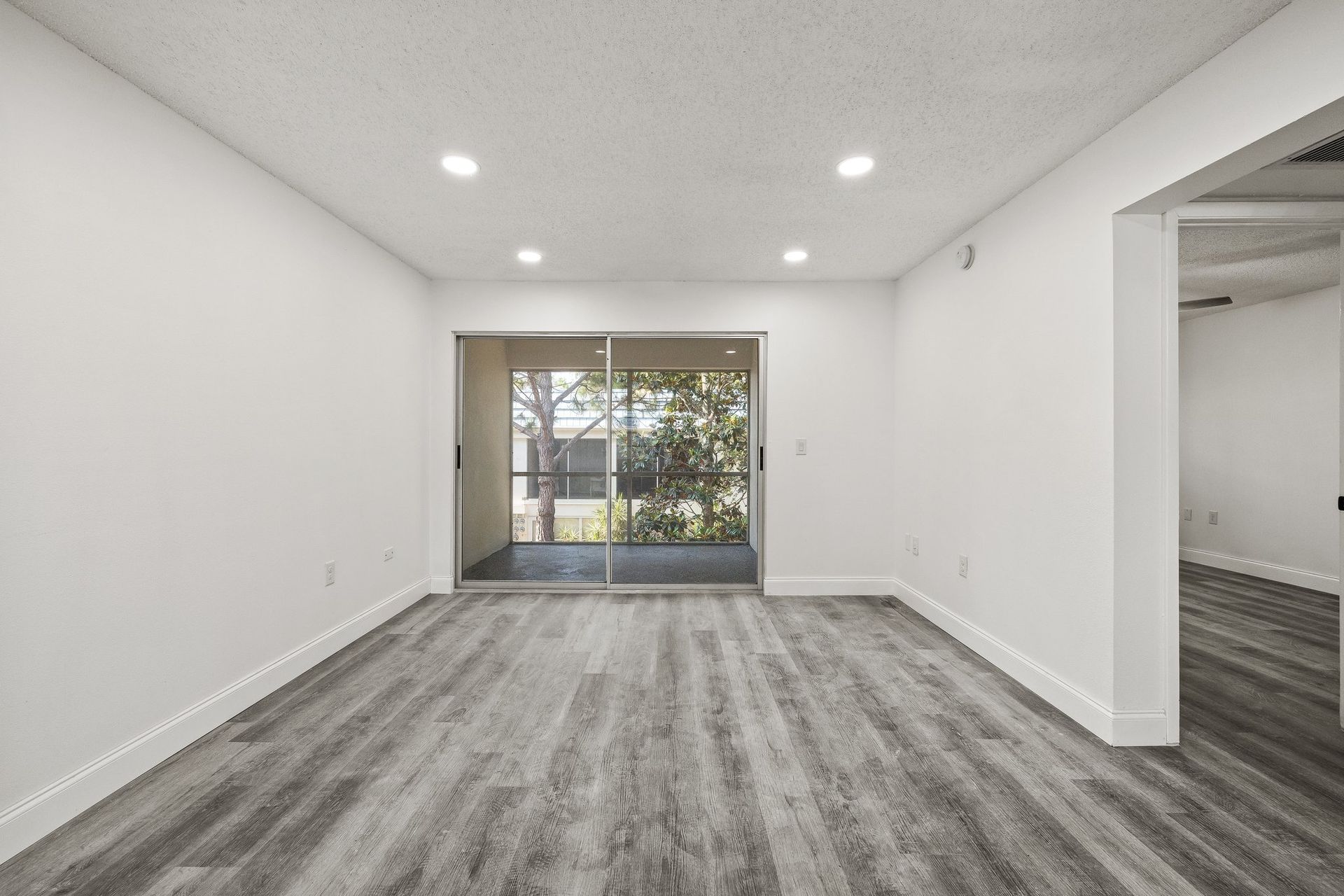 Empty white living room with gray wood floors and sliding glass doors to a balcony