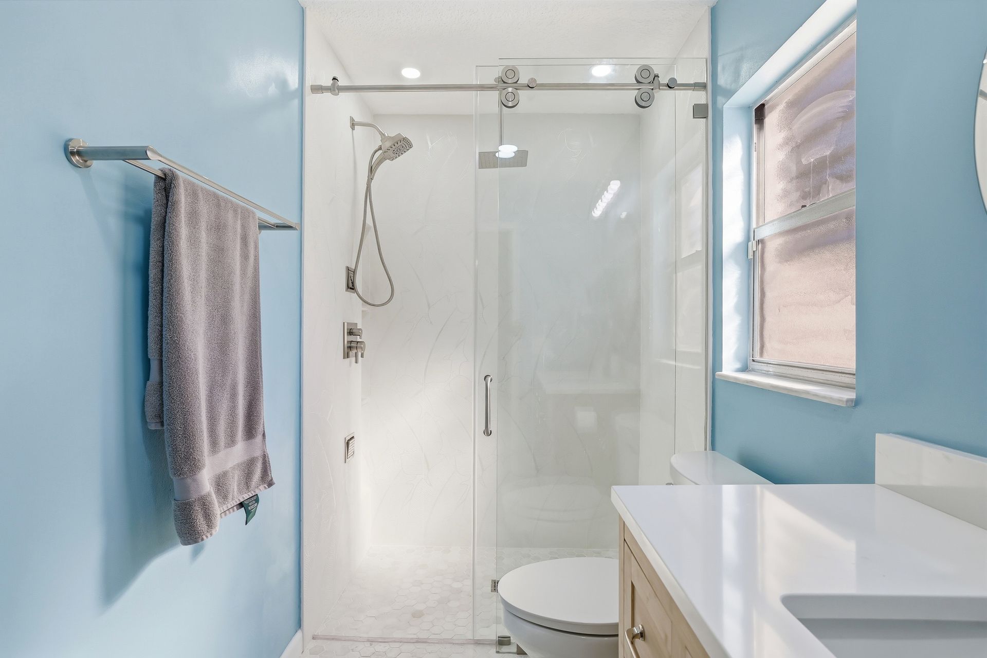 Bright blue bathroom with glass shower, towel rack, and white vanity by a window