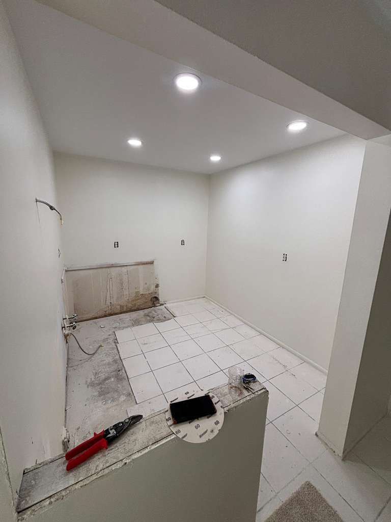 Partially renovated empty white room with tiled floor and tools in the foreground