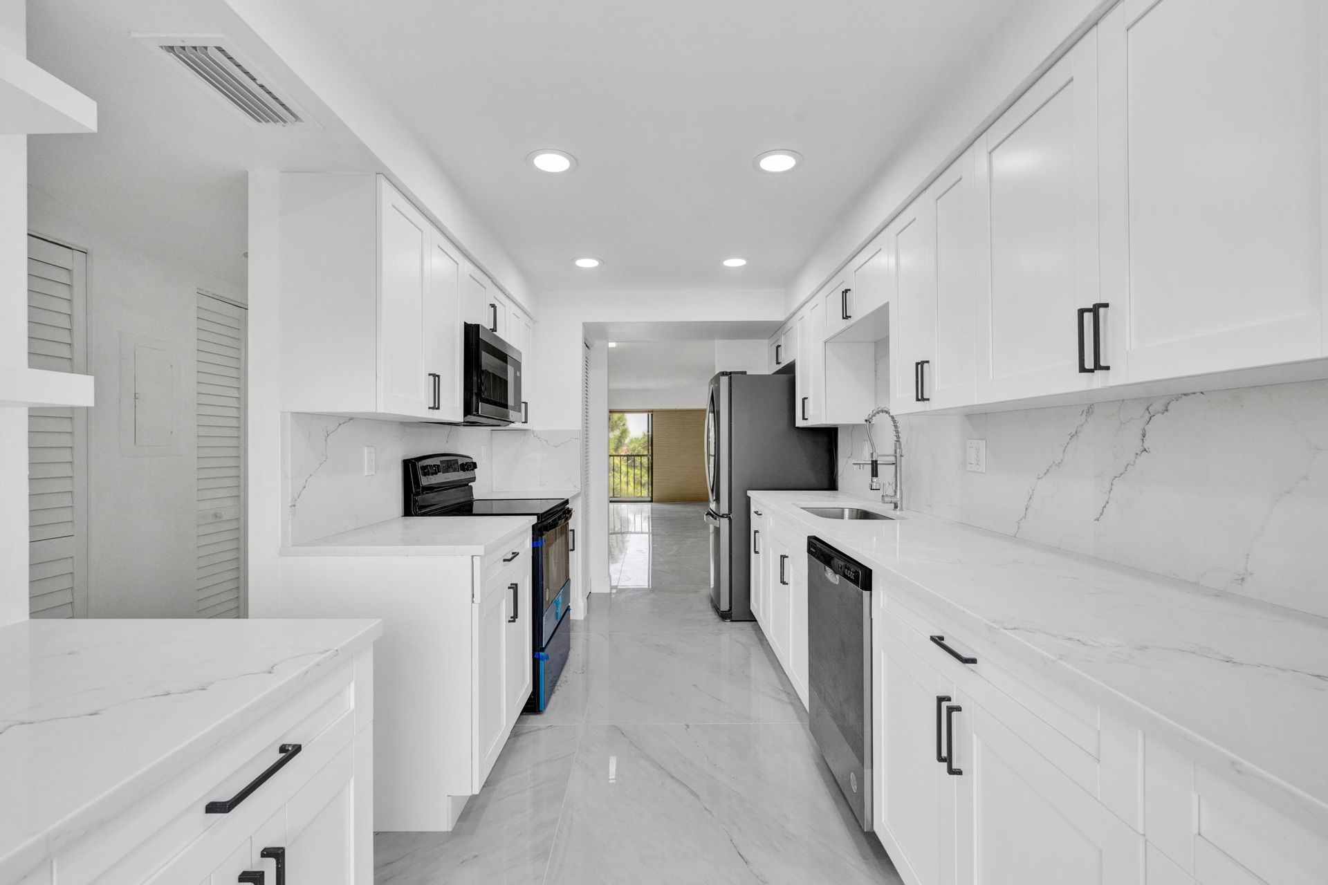 Bright modern white kitchen with marble counters, black handles, and stainless appliances