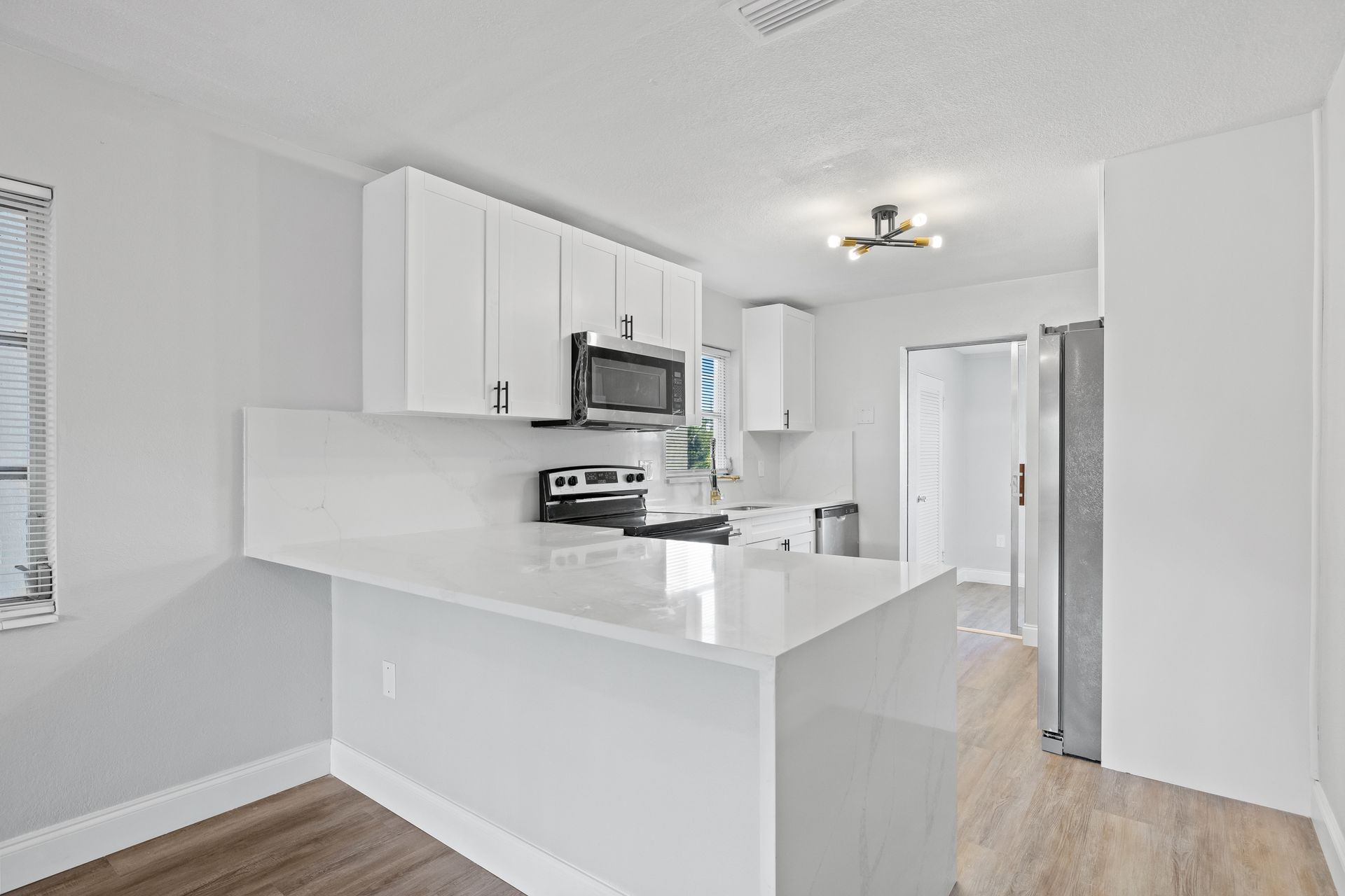 Bright white kitchen with peninsula, stainless appliances, and light wood floor in a small apartment
