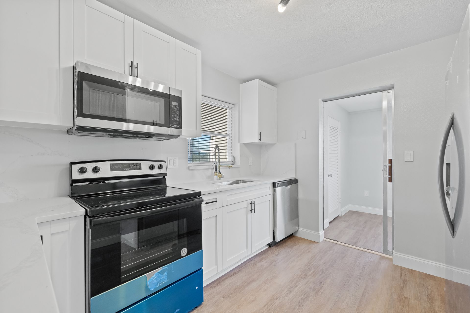 Bright white kitchen with black stove, stainless microwave, white cabinets, and light wood flooring