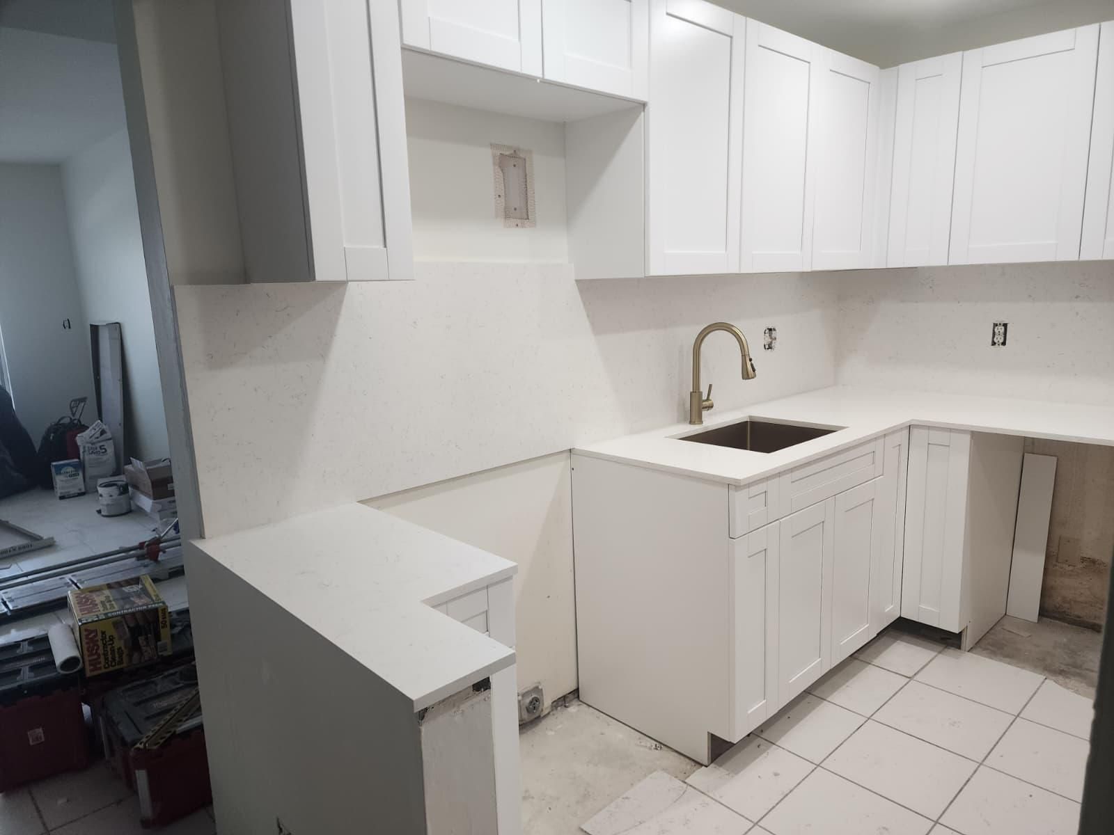 White L-shaped kitchen under renovation with cabinets, sink, and tiled floor