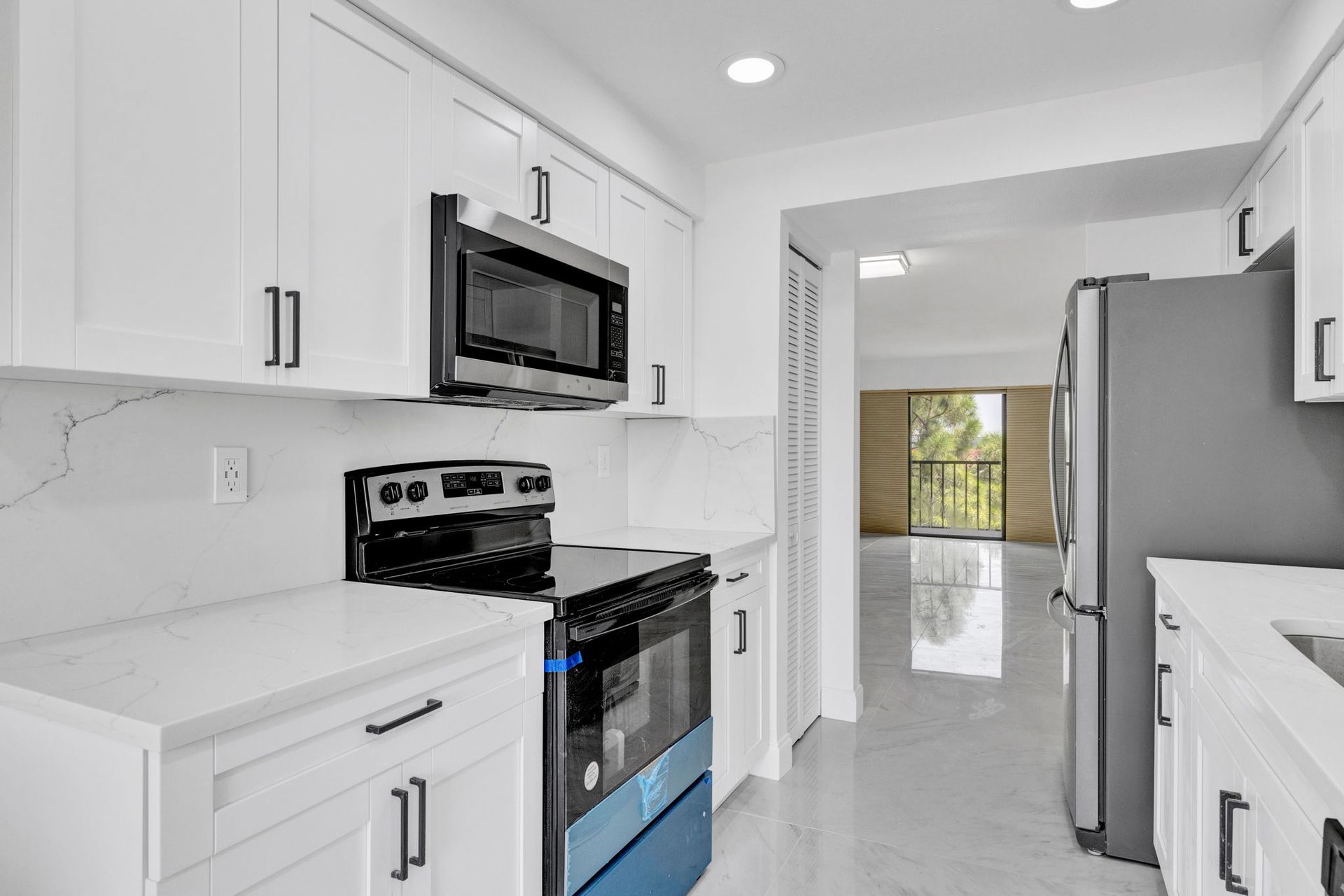 Bright white kitchen with stainless steel appliances and a view into a dining area.