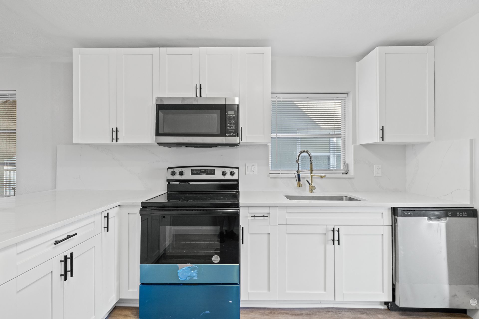 Bright white kitchen with stainless appliances, black stove, and sink under a window