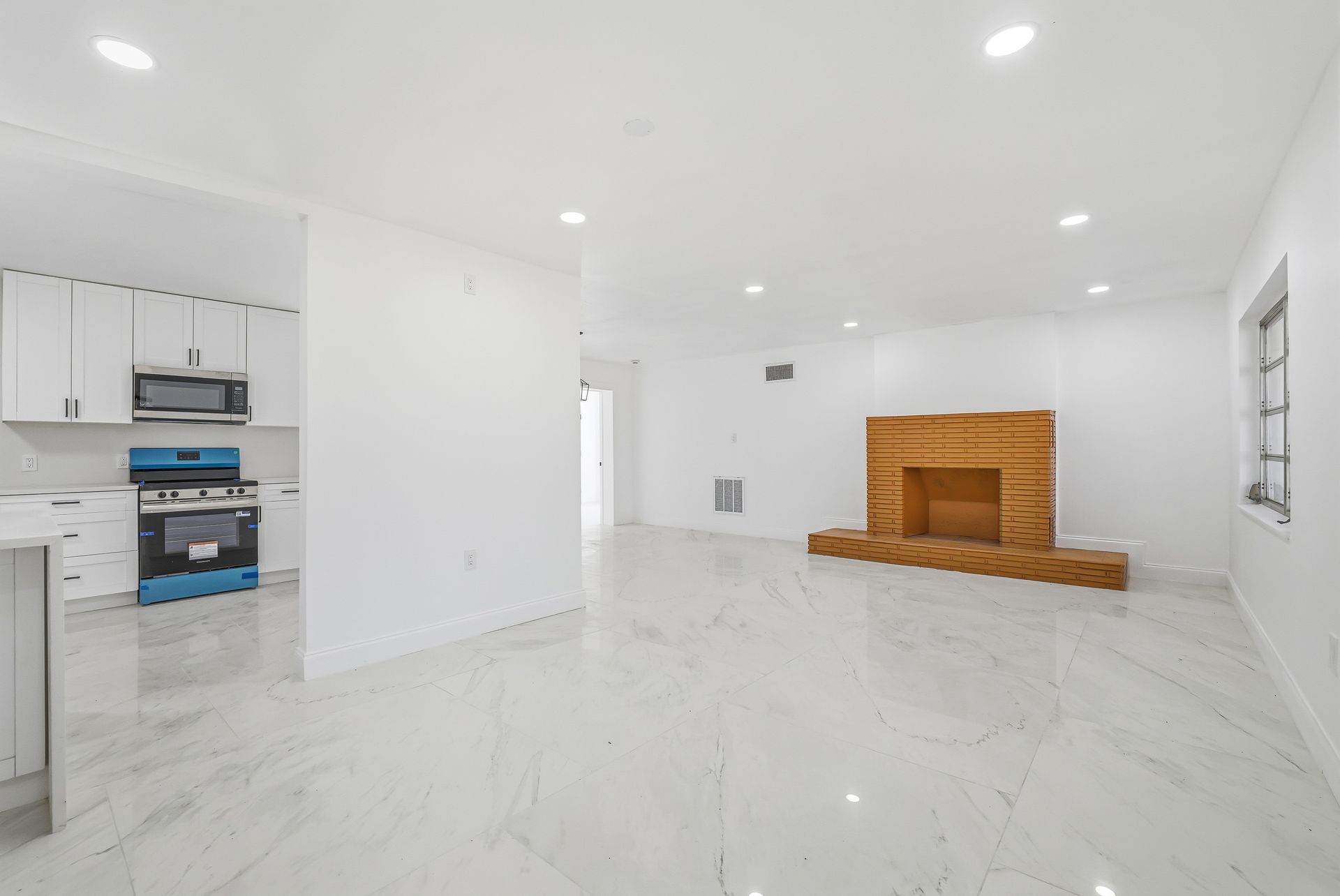 Bright empty living room with white tile floors, recessed lights, and a wood fireplace