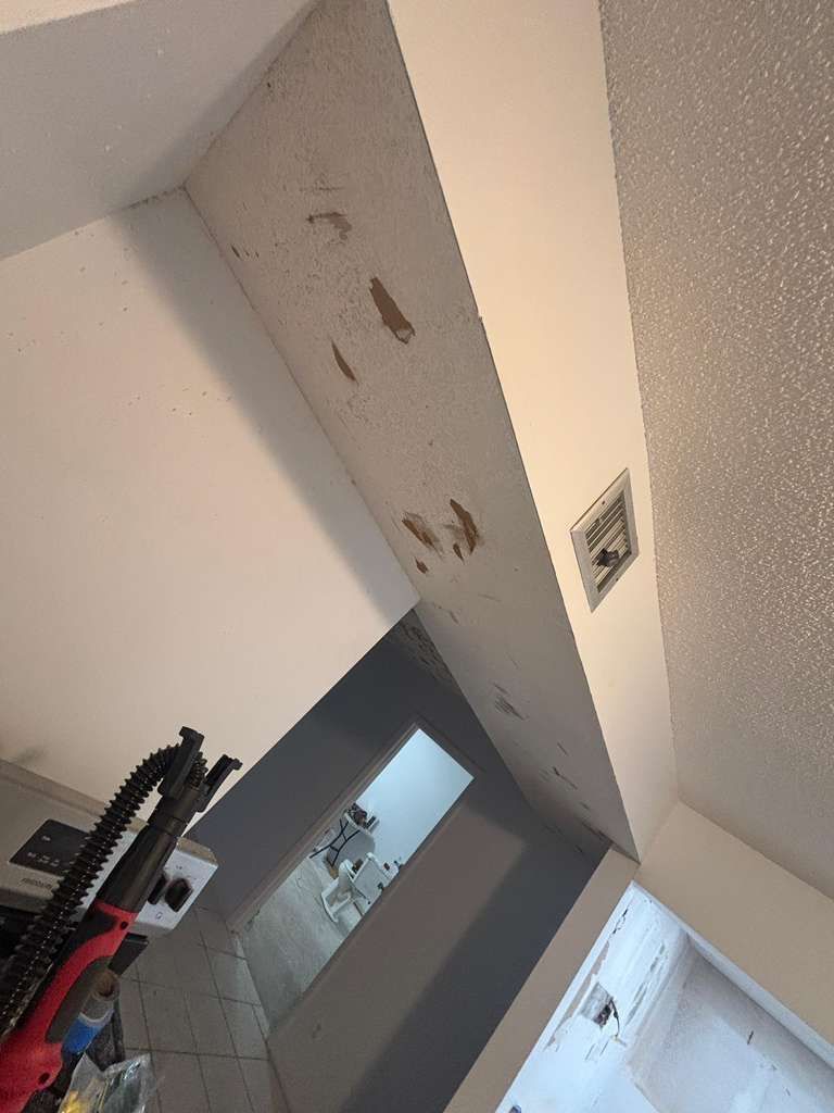 Ceiling with water stains above a hallway and open doorway, with a gym machine at left.