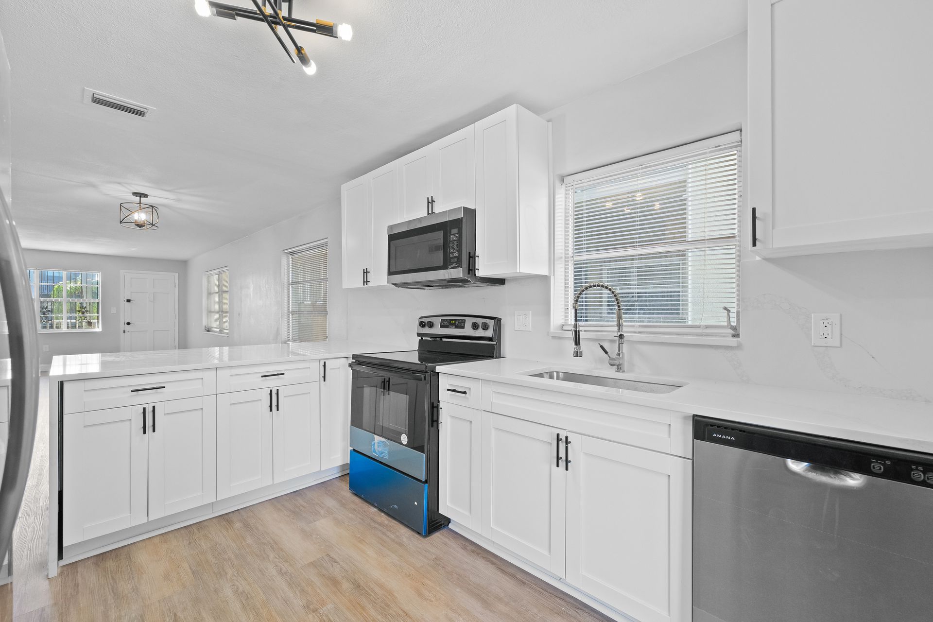 Bright white modern kitchen with stainless steel appliances, white cabinets, and light wood flooring