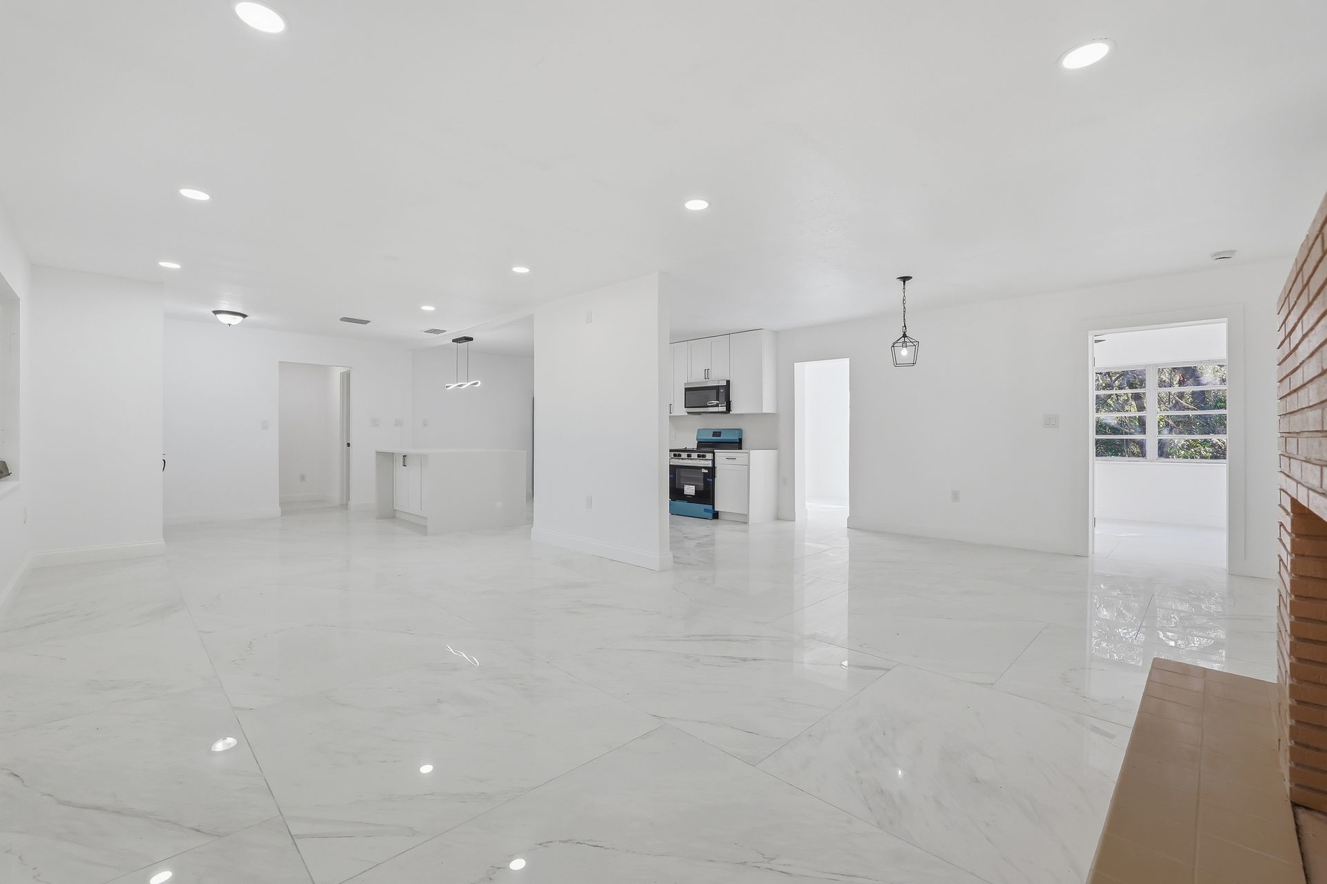 Bright empty modern room with glossy white tile floors, recessed lights, and a small kitchen area.