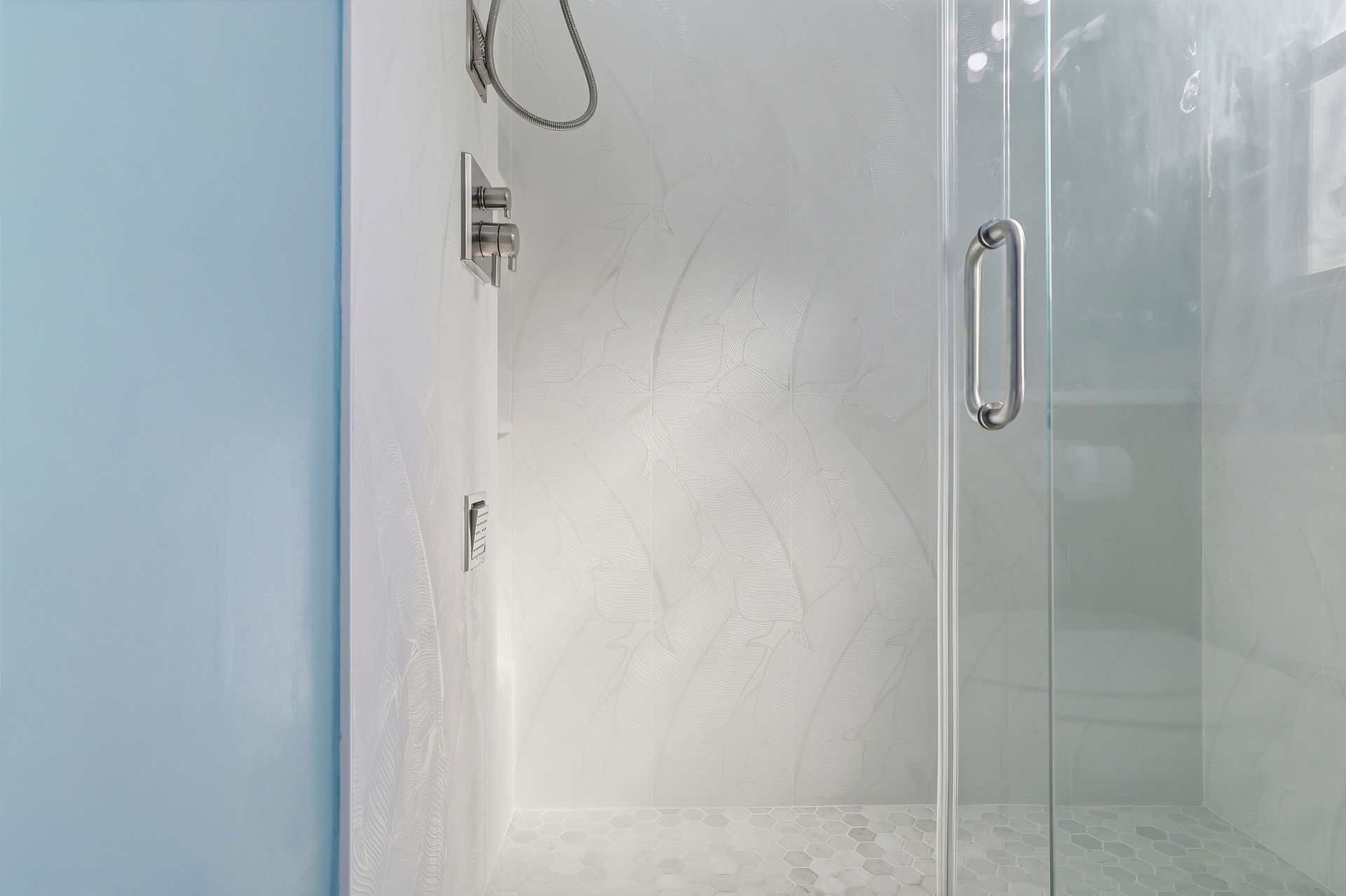 Modern glass shower enclosure with a chrome handle in a white-tiled bathroom