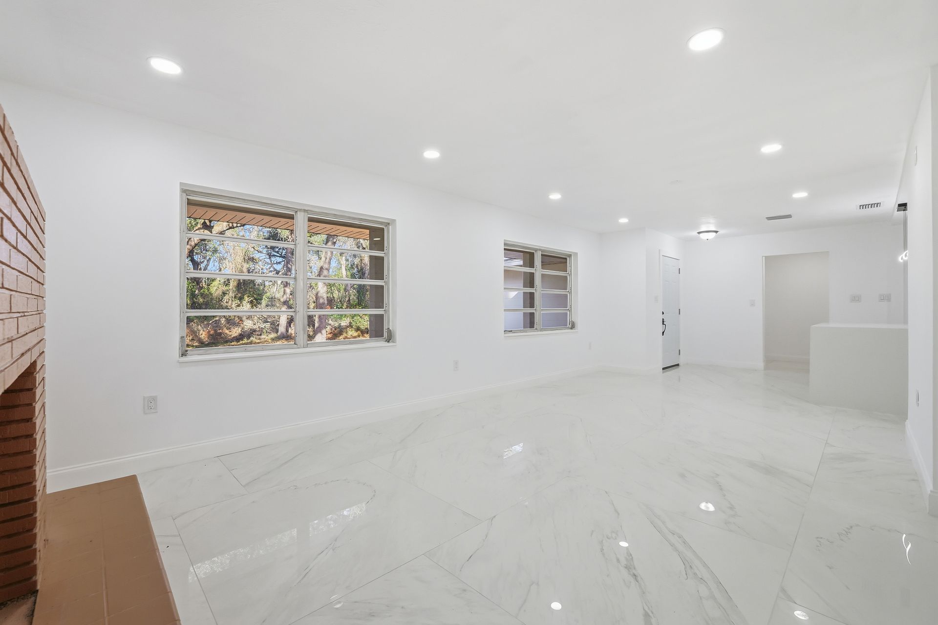 Bright empty white room with glossy tile floor, recessed lights, and windows looking outside