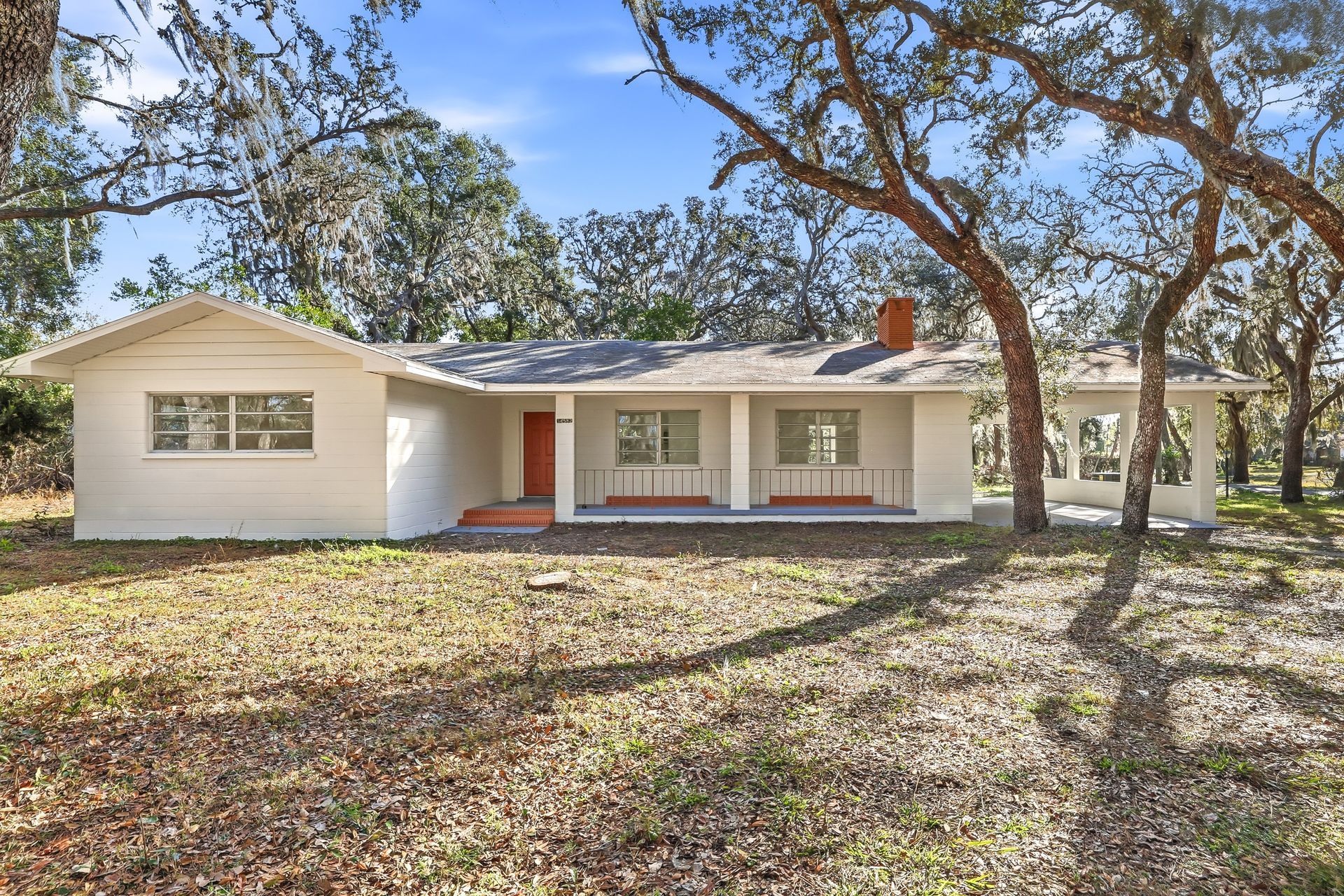 Single-story white house with a front porch, trees, and a leaf-covered yard
