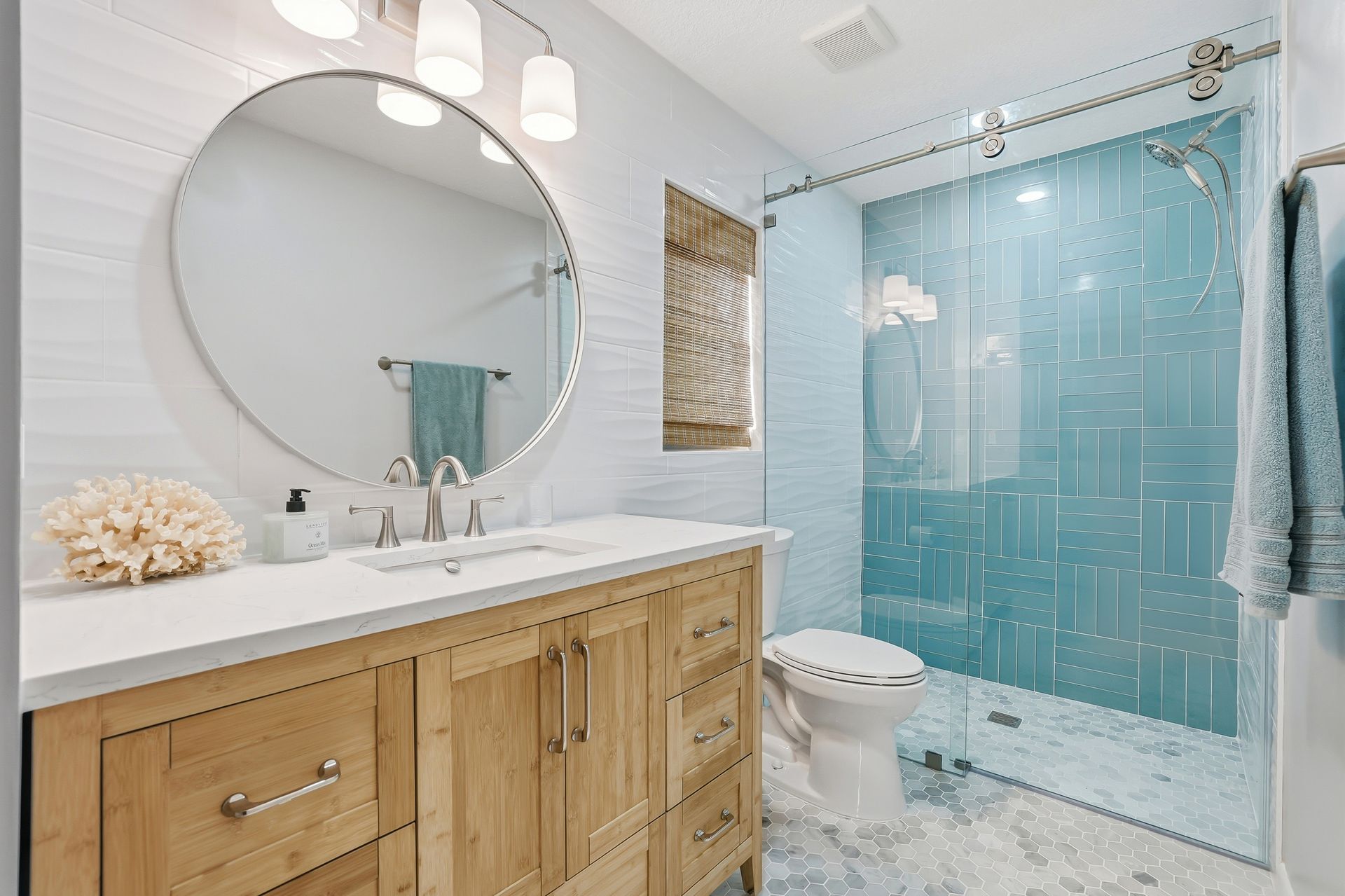 Bright bathroom with wood vanity, round mirror, and blue glass shower curtain
