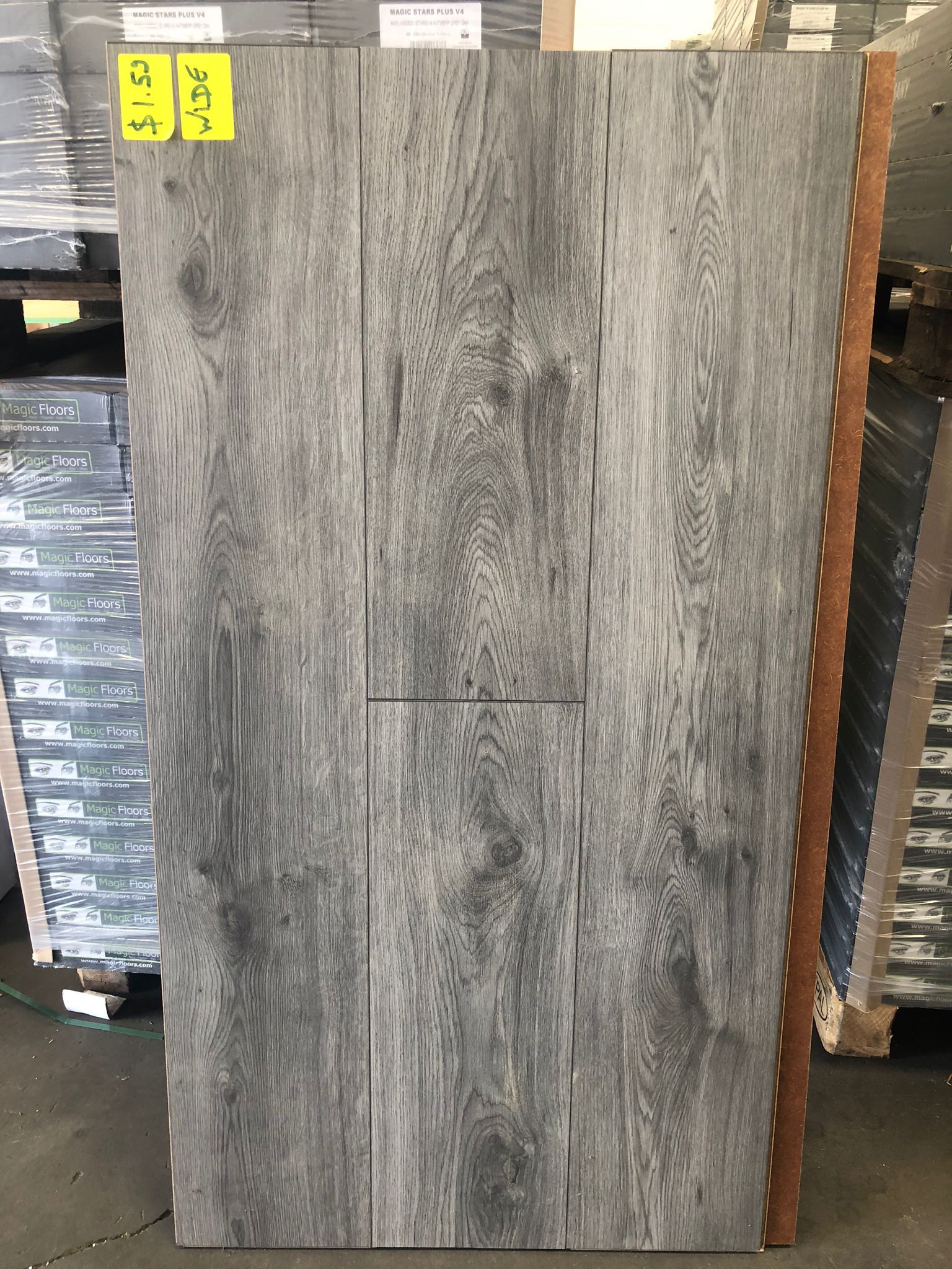 Gray wood-look tile slab standing in a warehouse, with a small yellow label at the top left