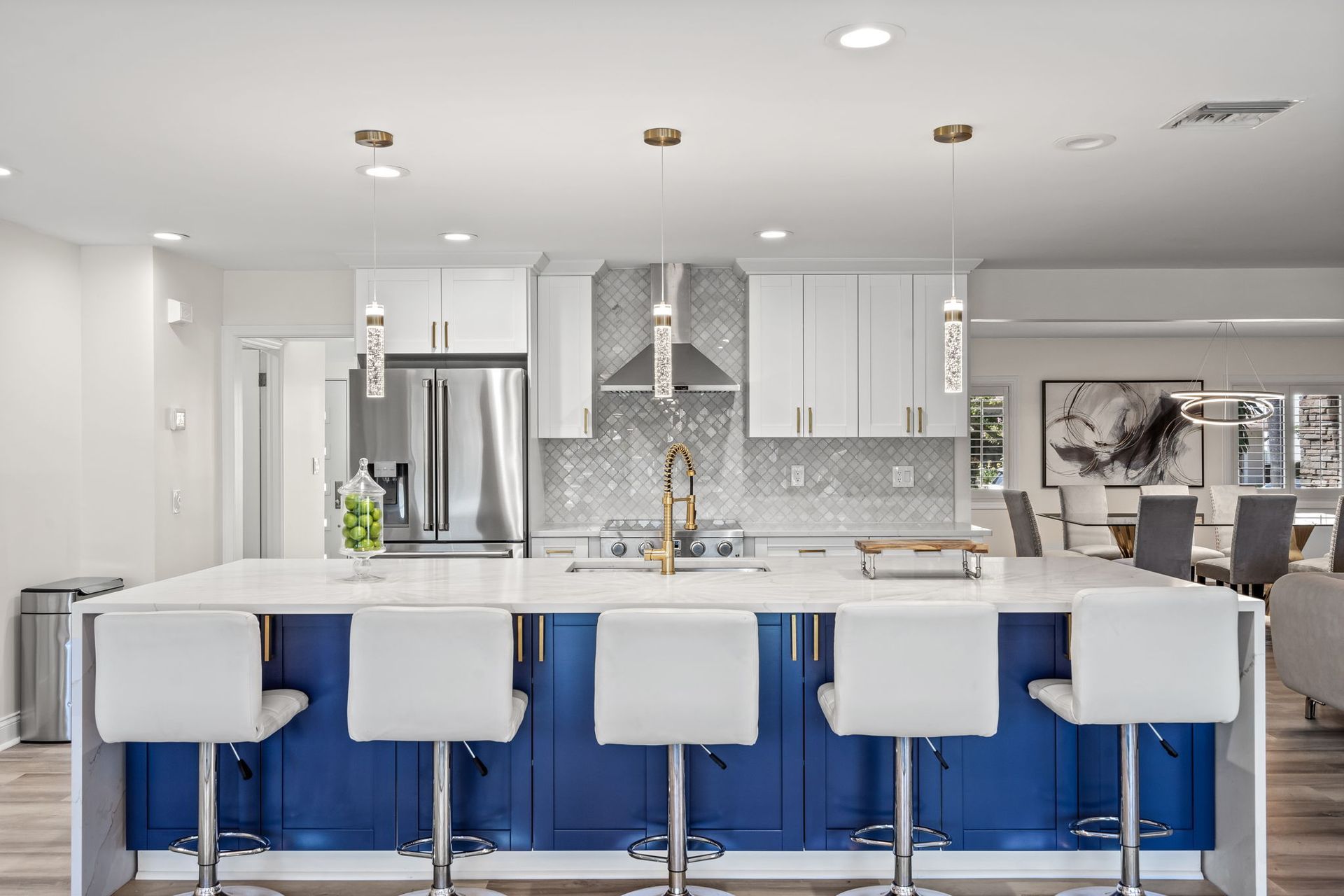 Modern white kitchen with blue island, four white stools, and stainless steel appliances