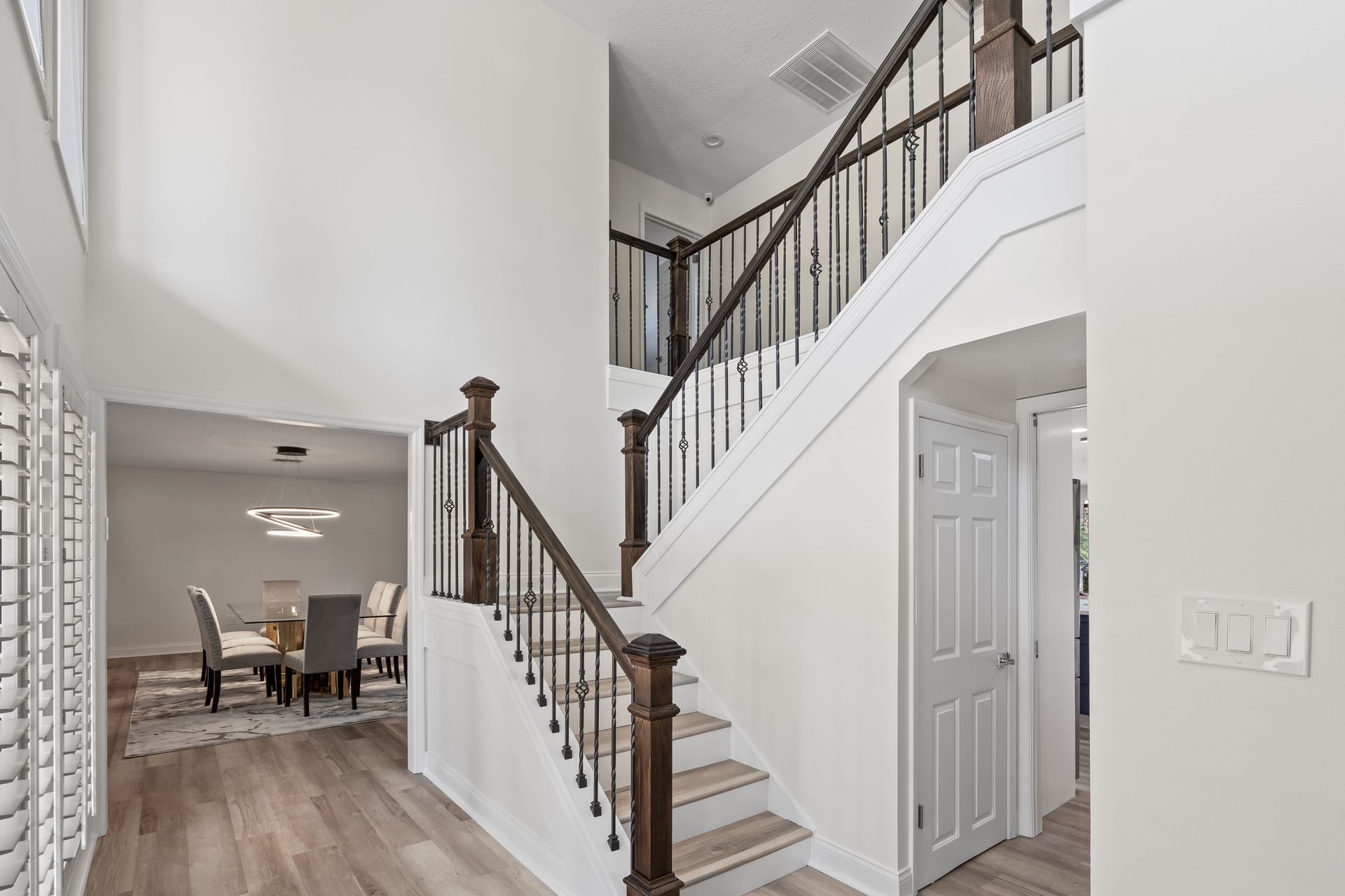 Bright foyer with staircase, white walls, dark railings, and open view to dining room