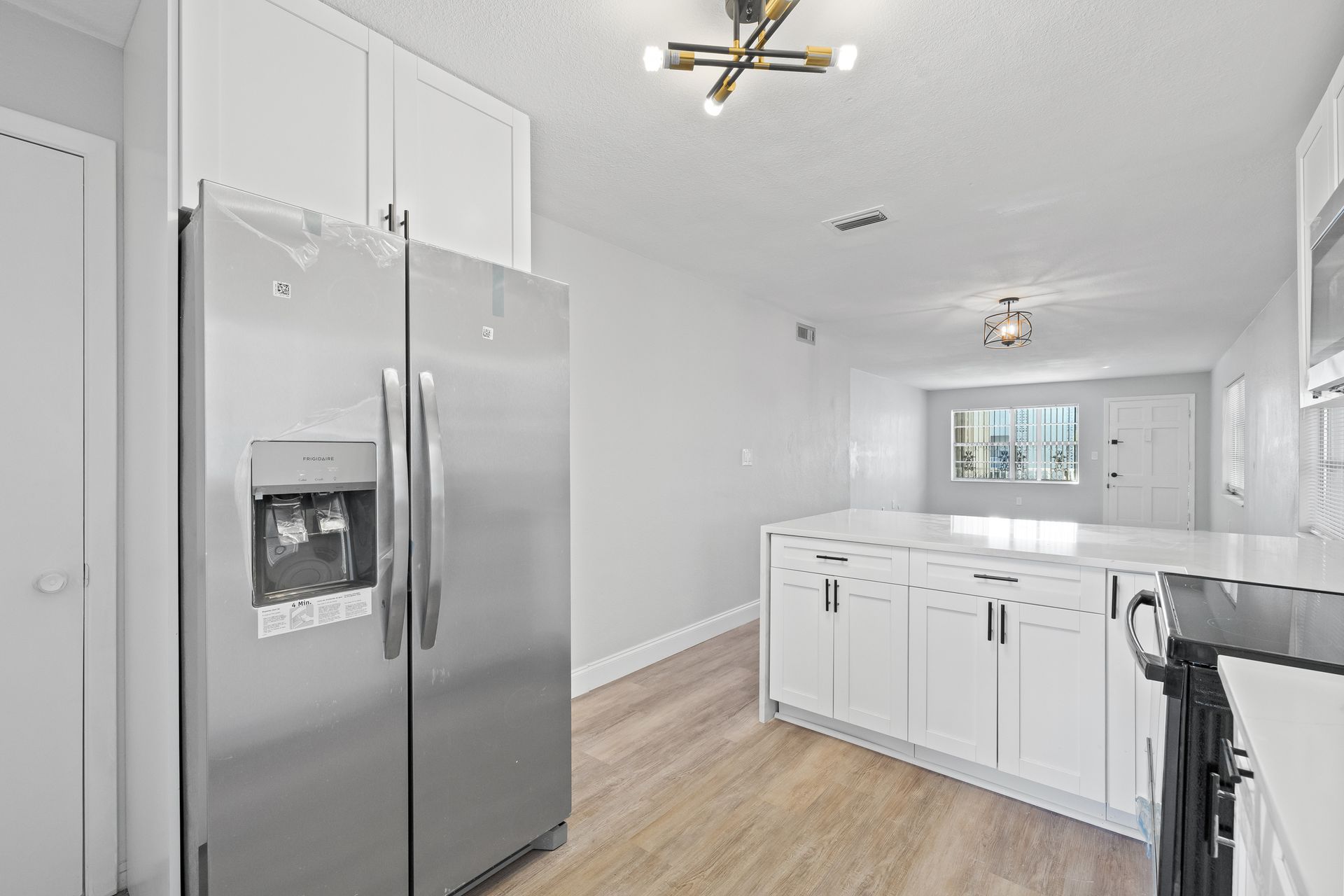 Bright white kitchen with stainless steel refrigerator, island, and wood floors, viewed from the entryway