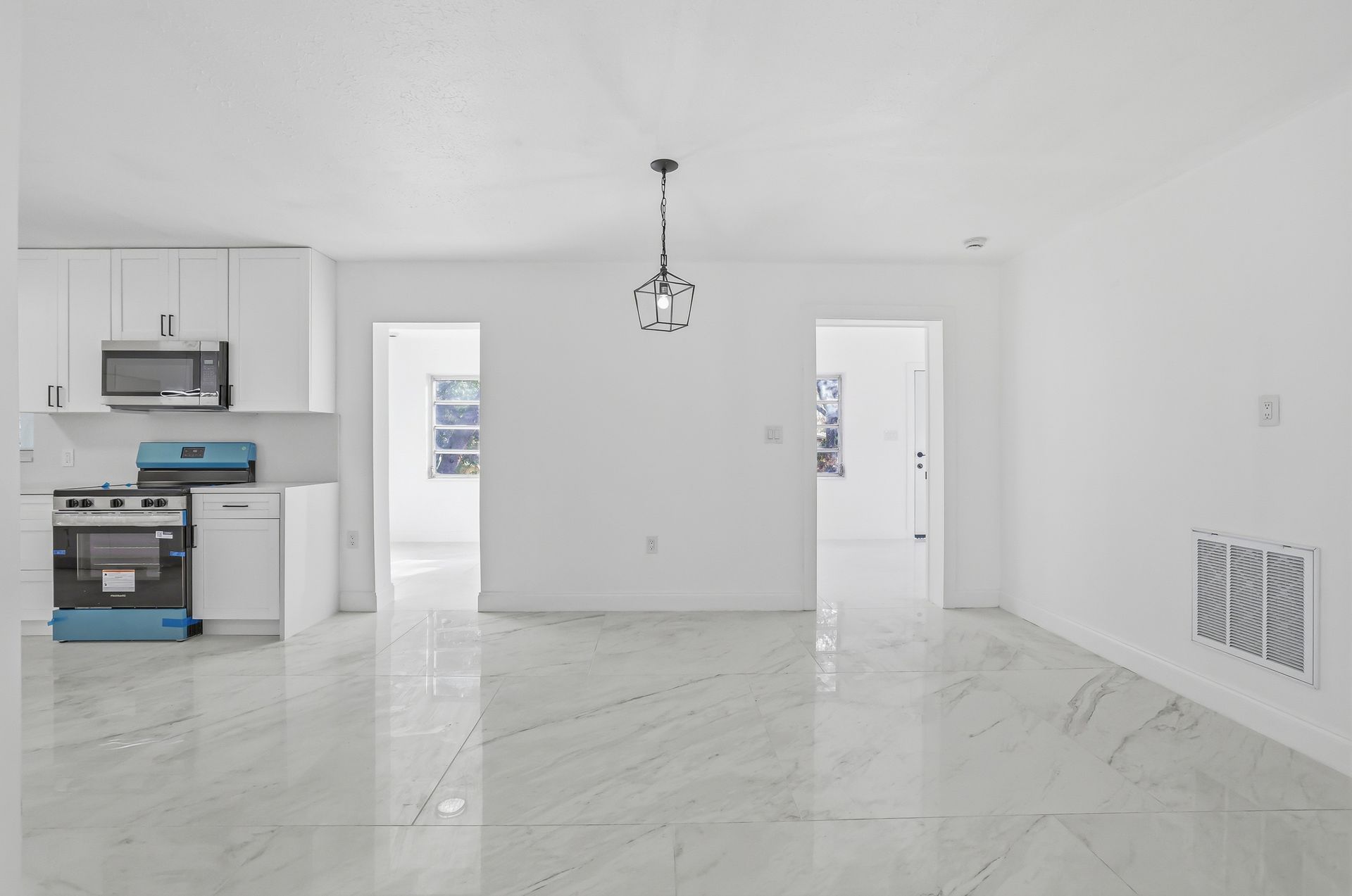 Bright empty white kitchen and living area with marble floors and pendant light, seen from the main room