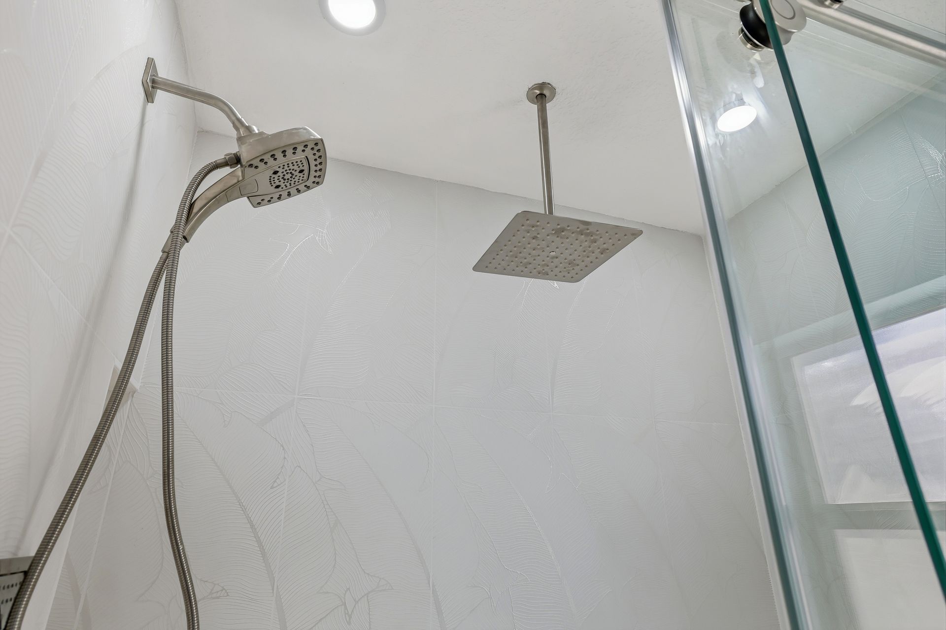 Bathroom shower with wall-mounted showerhead, hose, and square rainfall head near a glass enclosure