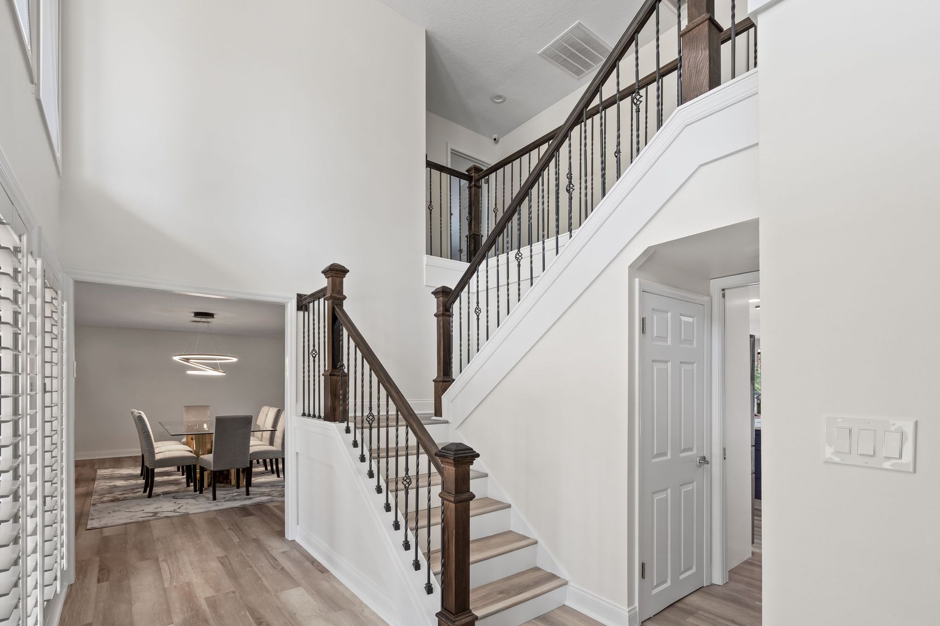 Bright entryway with a white staircase, dark wood railing, and dining room visible in the background