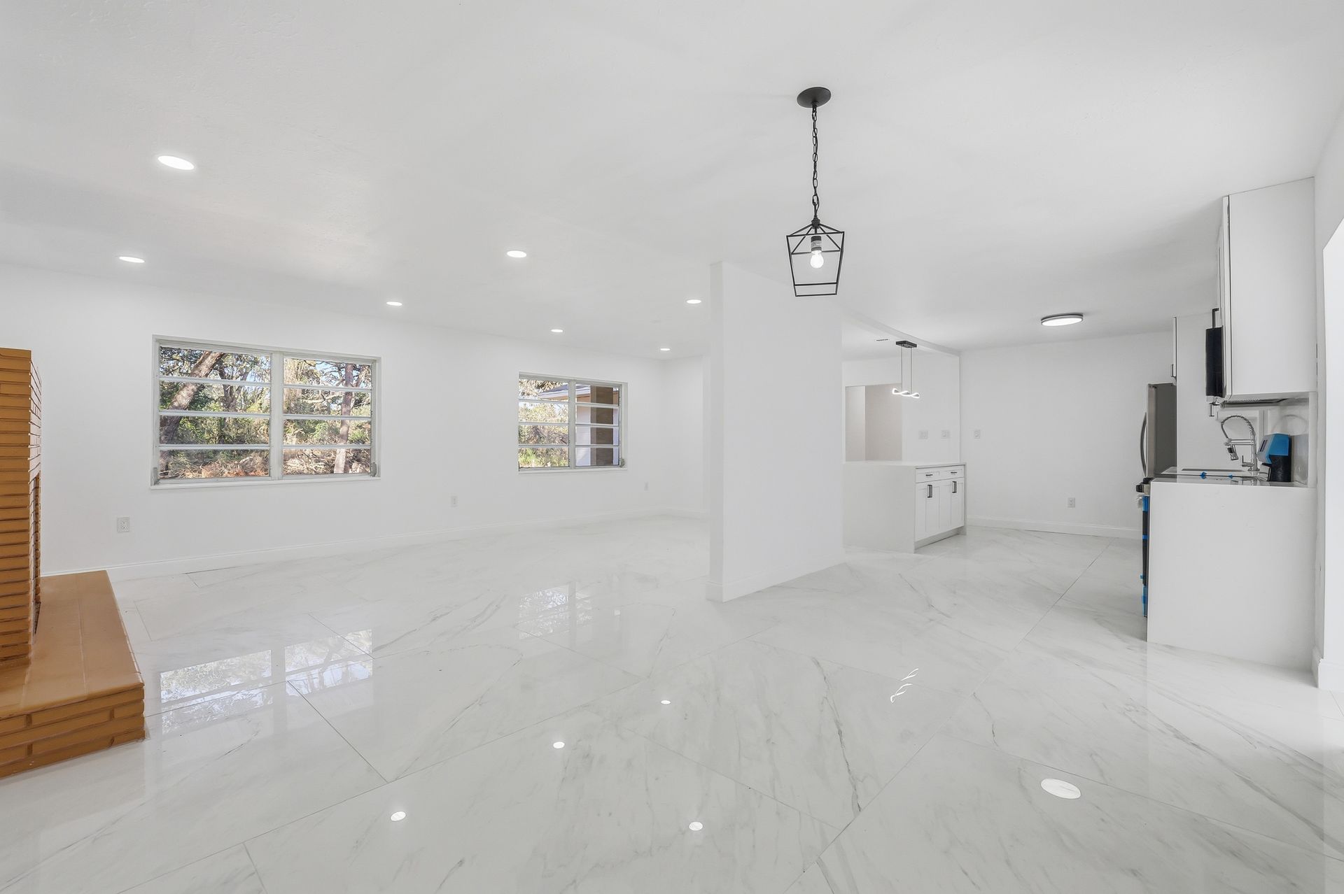 Bright empty modern living room with glossy white floors, recessed lights, and kitchen area on the right
