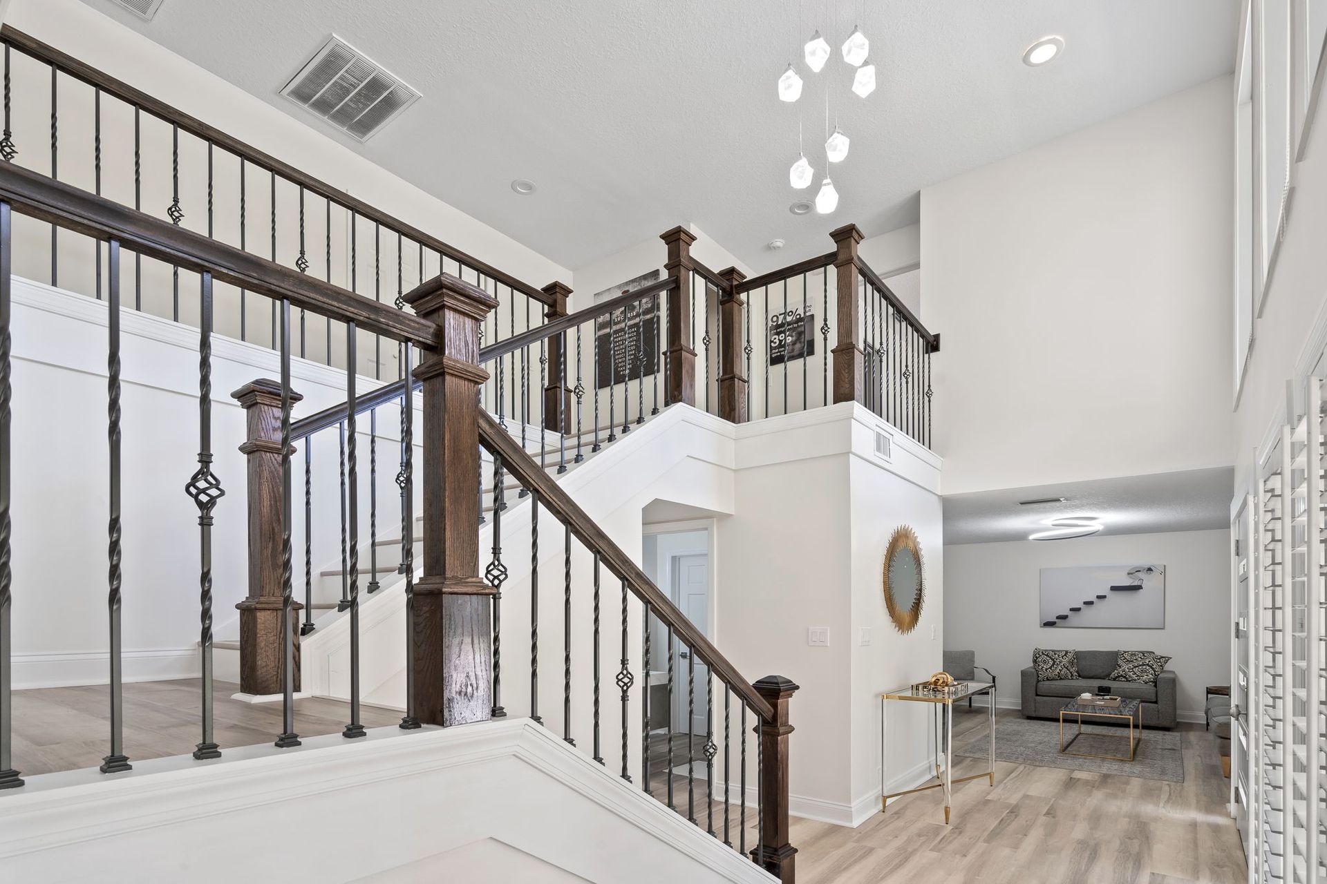 Bright foyer with staircase, white walls, wood floors, and a glimpse of living room seating beyond.