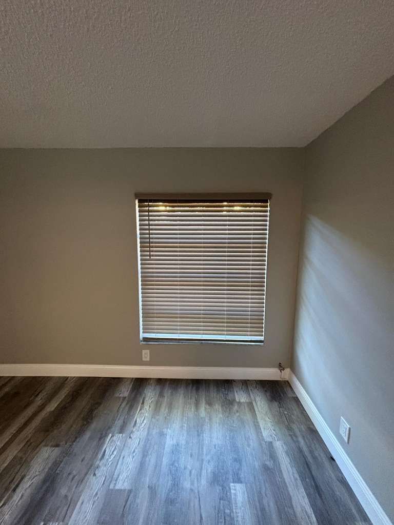 Empty room with wood flooring, gray walls, and a window with blinds.
