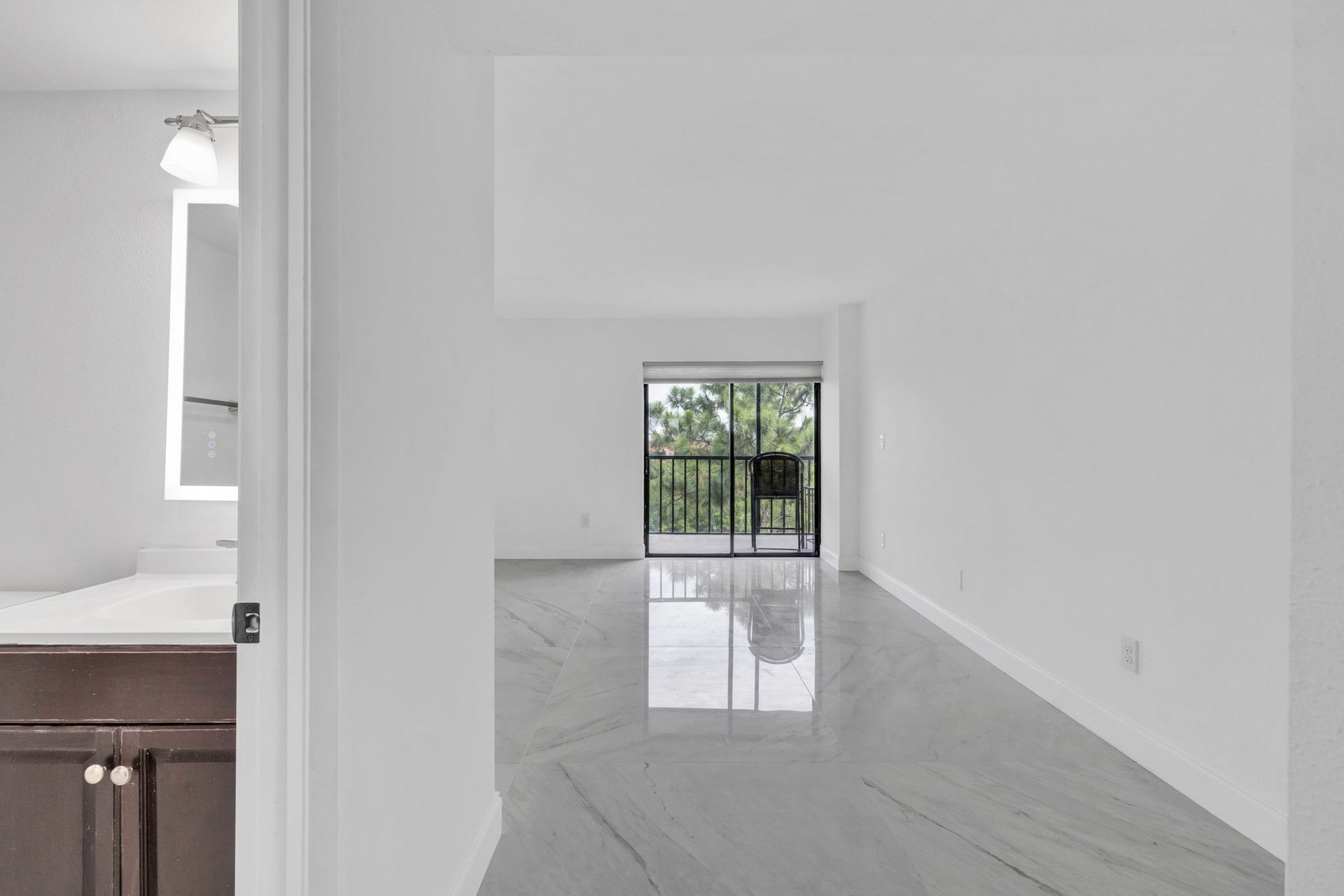 Bright empty room with glossy tile floor, white walls, and a small window view of greenery